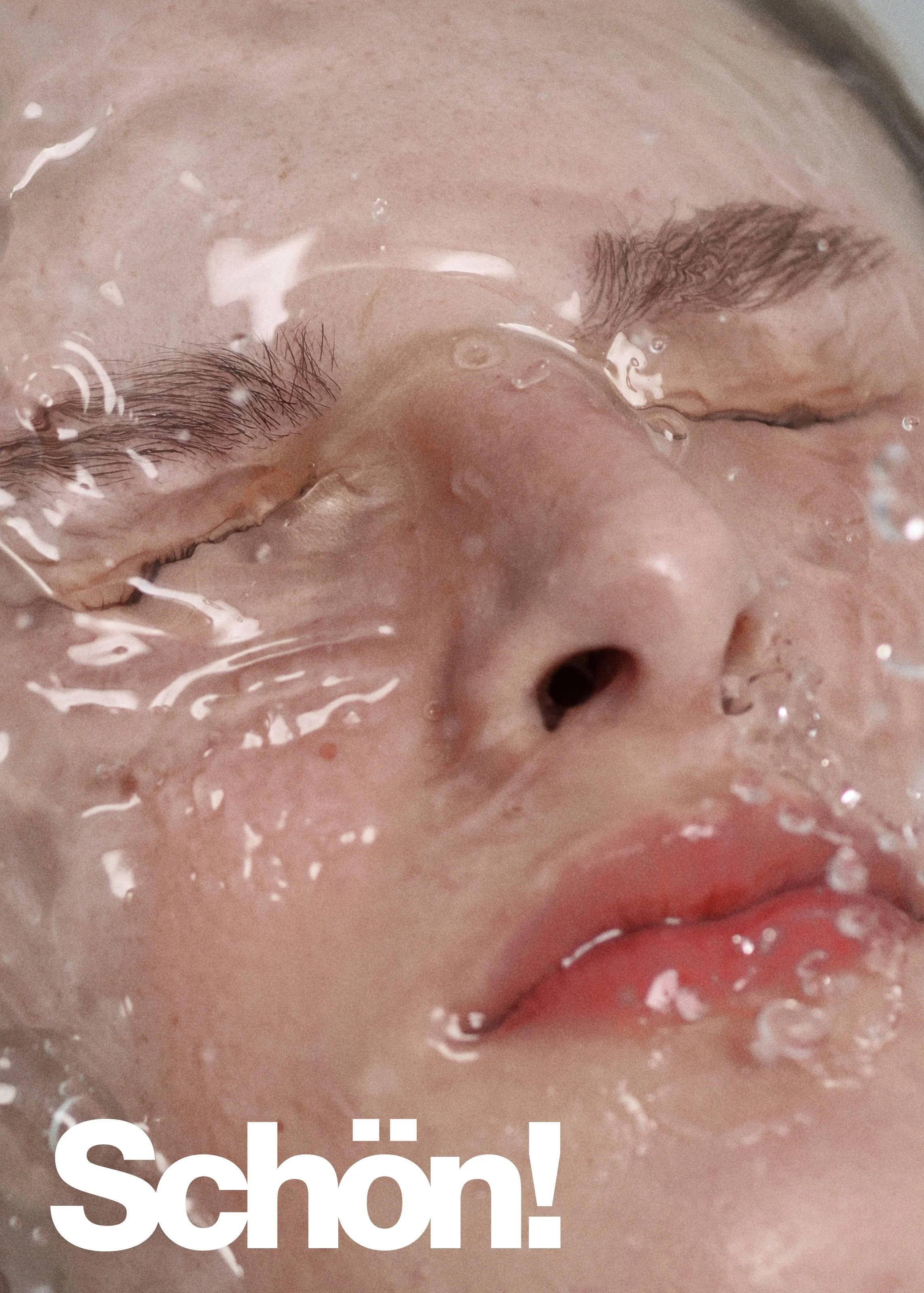 Close-up of a person with closed eyes and slightly parted lips, submerged in water with bubbles and ripples, with the word 'Schön!' in white at the bottom.