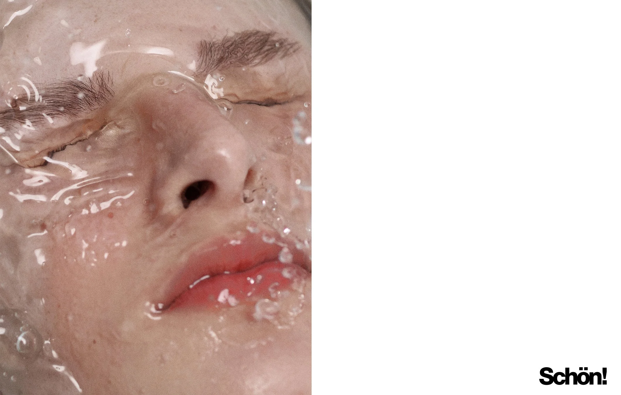 Close-up of a person's face with eyes closed, submerged in water, with water droplets on the skin and lips.
