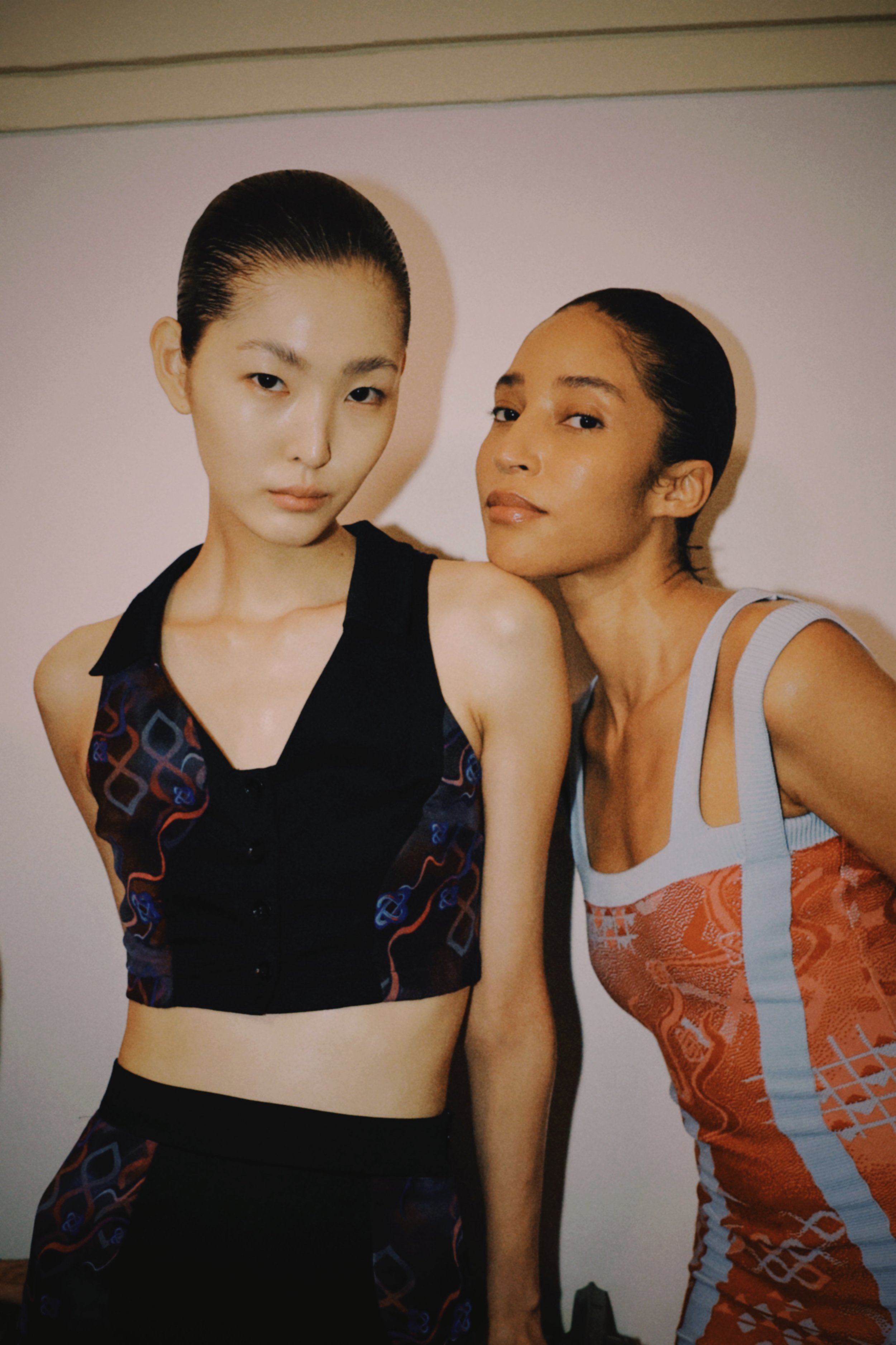 Two women with sleek hairstyles posing closely together for a photo against a plain background.