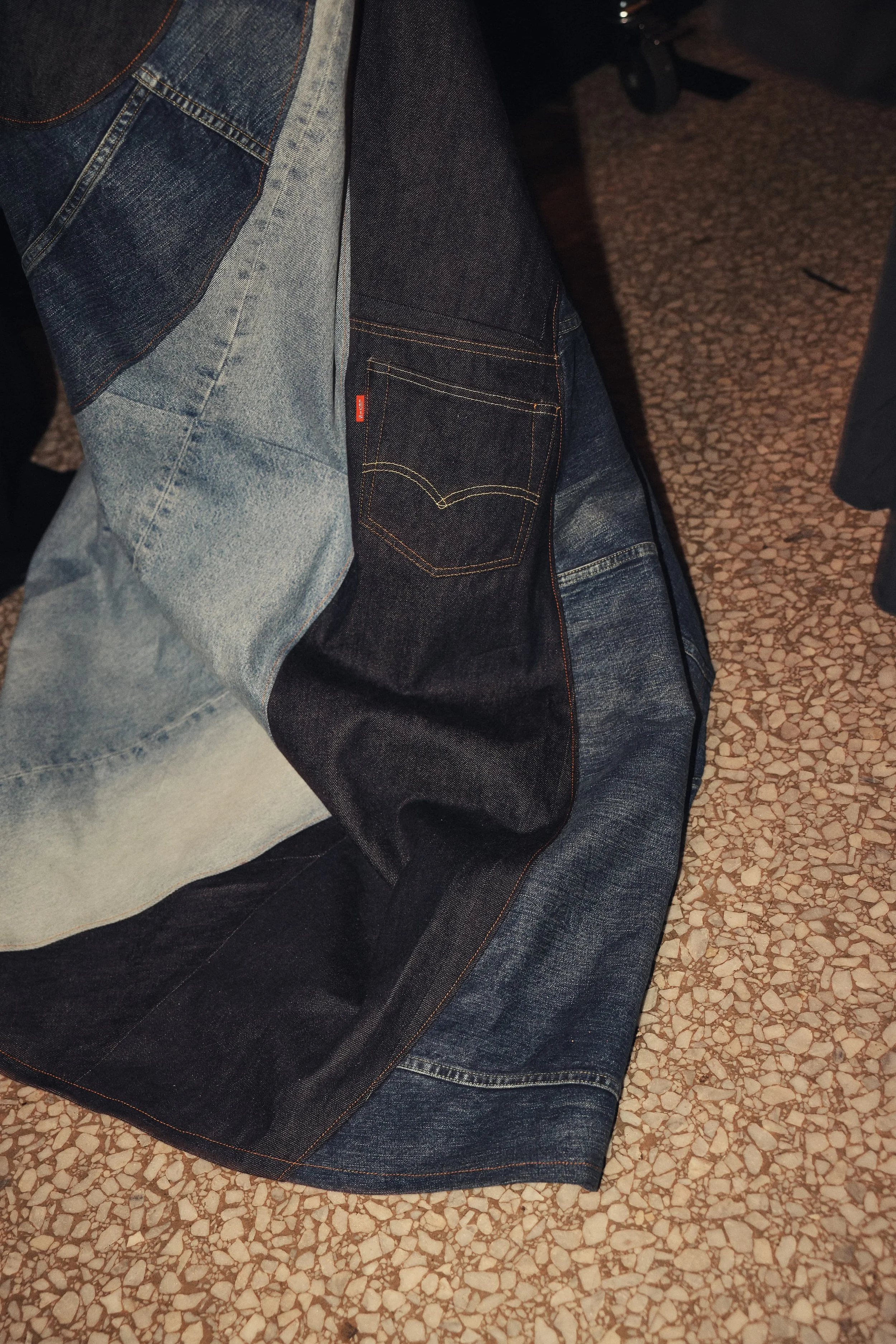 Close-up of a person wearing a patchwork denim jacket and jeans, sitting on a textured floor.