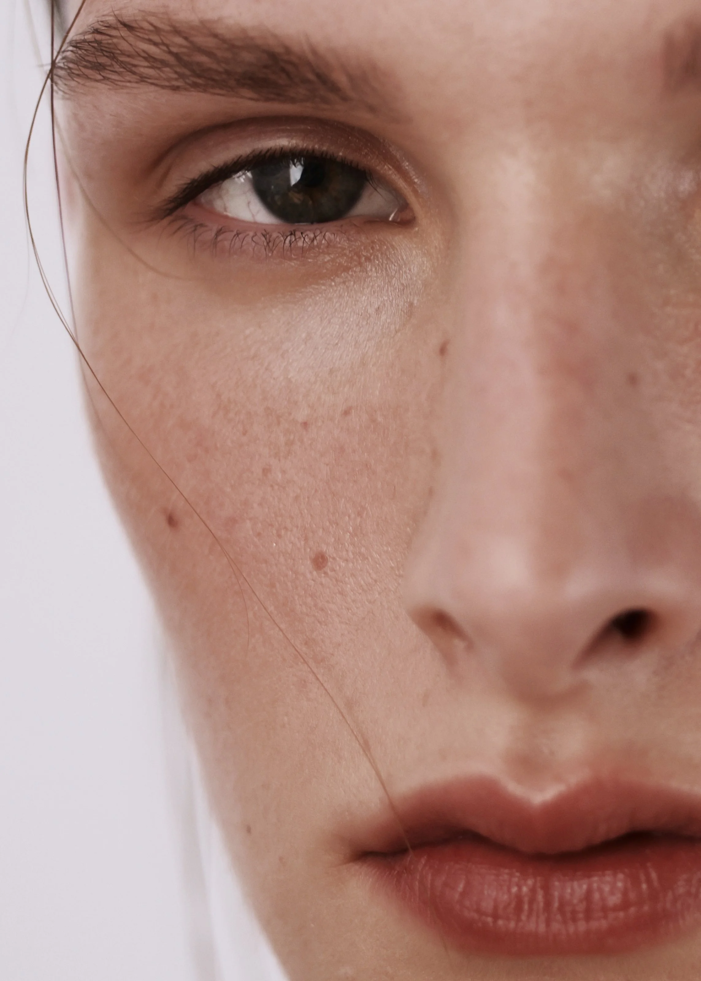 Close-up of a woman's face showing part of her eye, nose, and lips with natural skin texture and freckles.