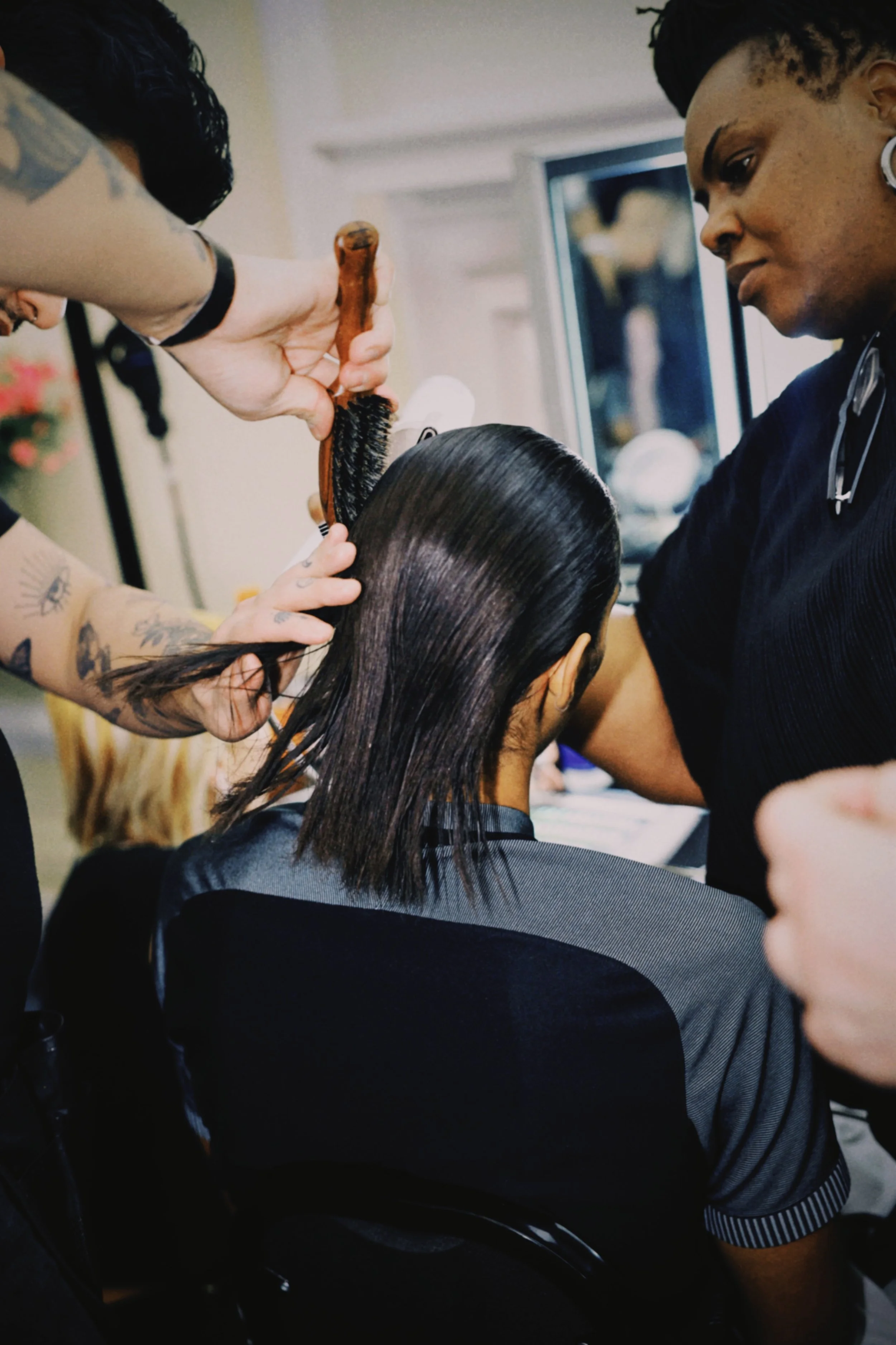 A hairstylist is blow-drying a woman's wet hair in a salon, with another stylist observing closely.
