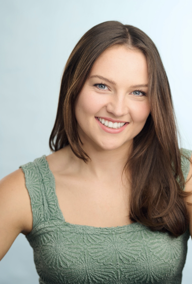Smiling person with long brown hair wearing a green textured top against a light blue background.