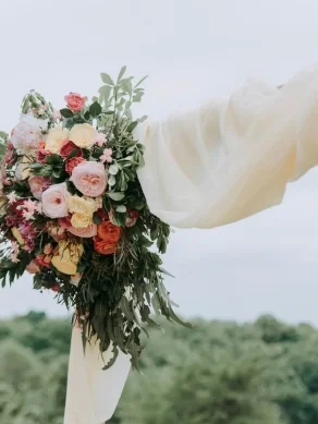 Wedding arch decorated with flowers and fabric outdoors against a natural backdrop.