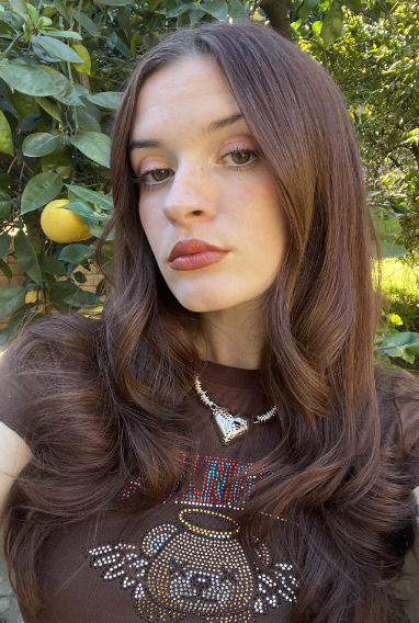 Person with long hair poses in front of a lemon tree.