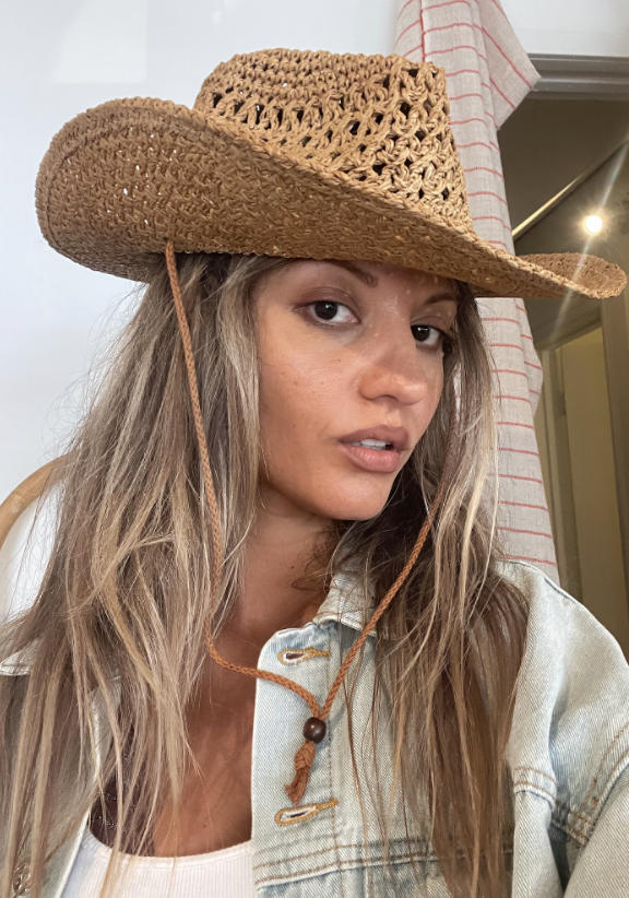 A woman wearing a straw cowboy hat and denim jacket indoors.