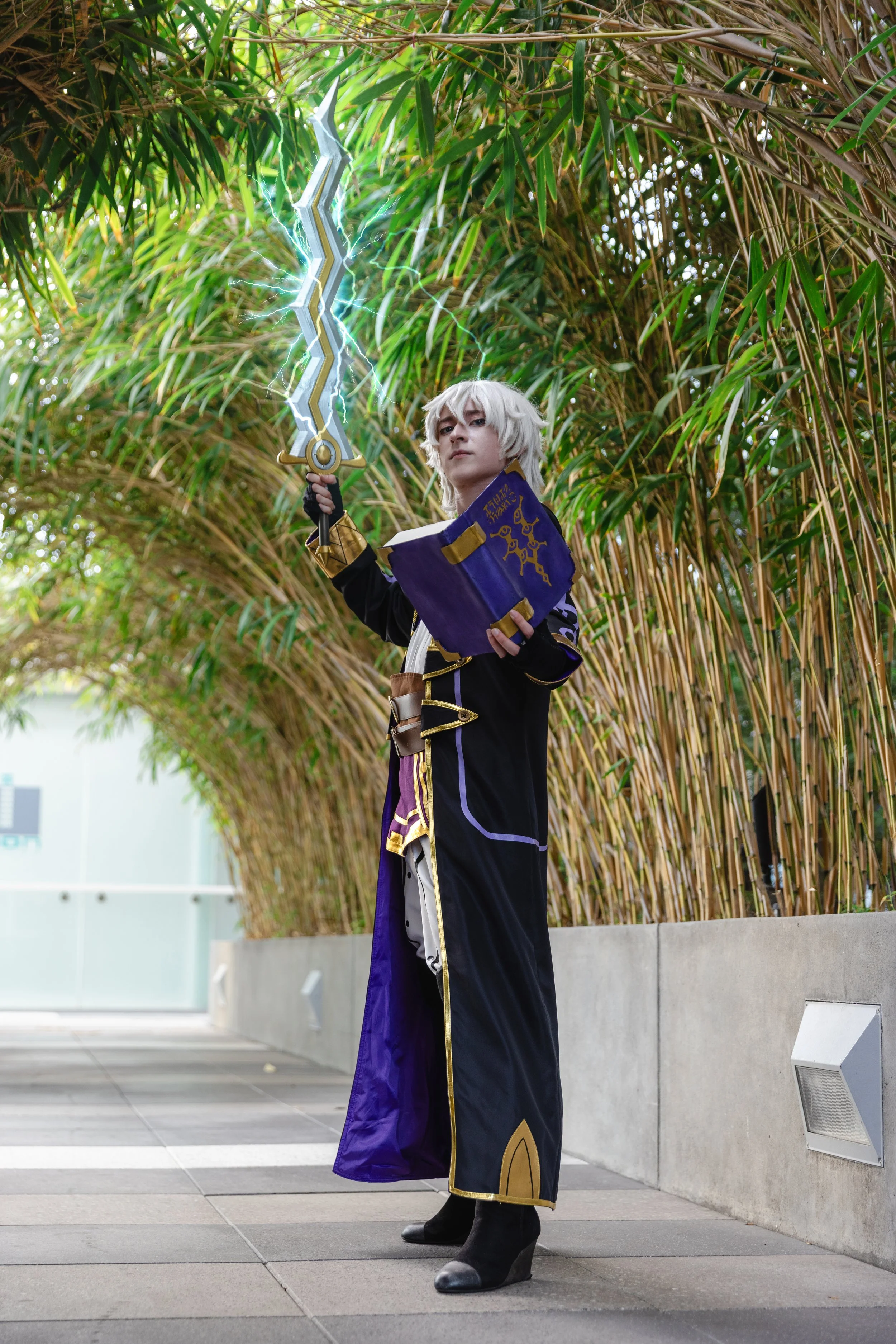 Person in cosplay costume standing outdoors, holding a large sword with lightning effects and a book, with bamboo trees and modern building in background.