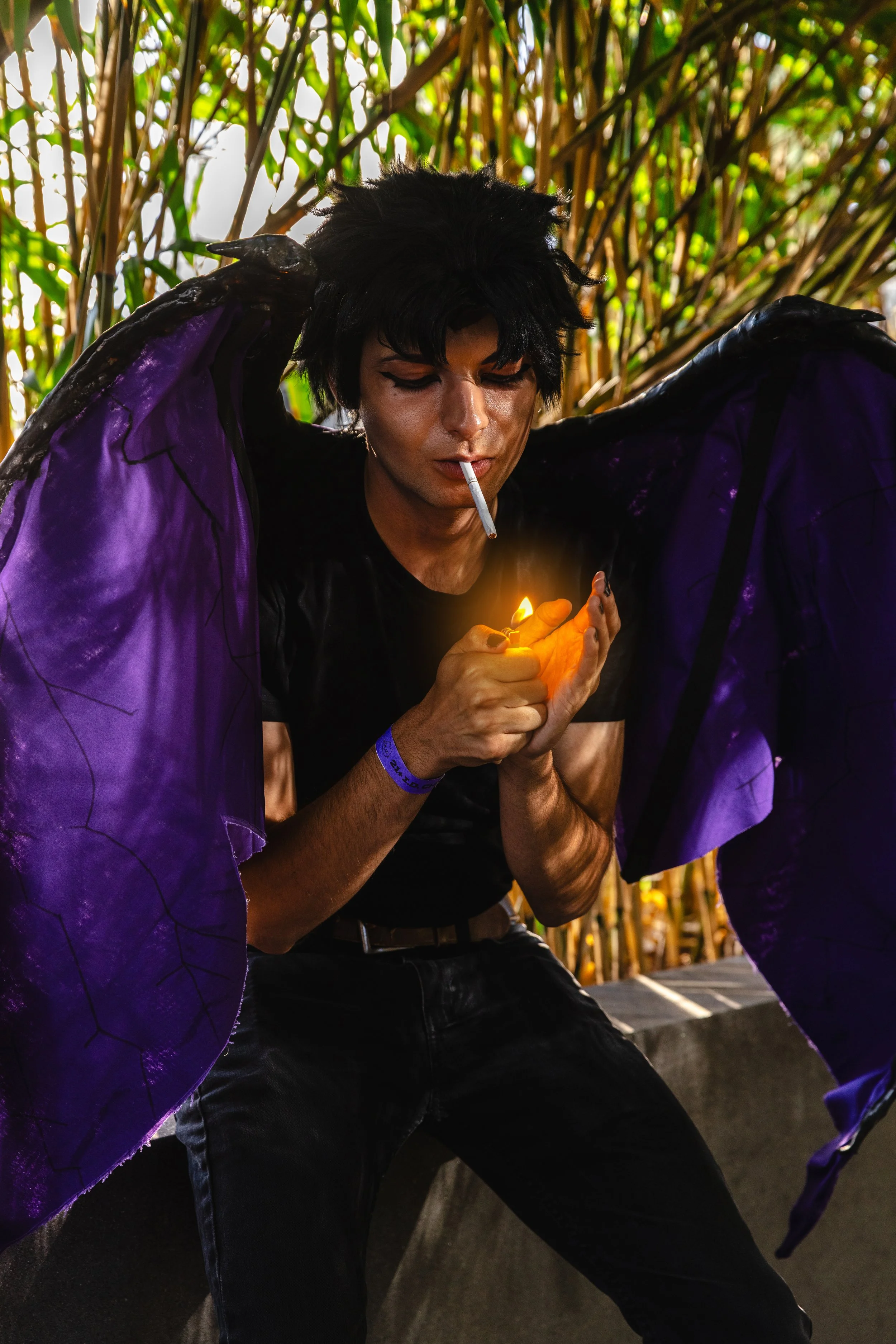 A person with black hair wearing a black shirt, purple wings, and a blue wristband, smoking a cigarette, and holding a lit lighter, with a background of bamboo plants.