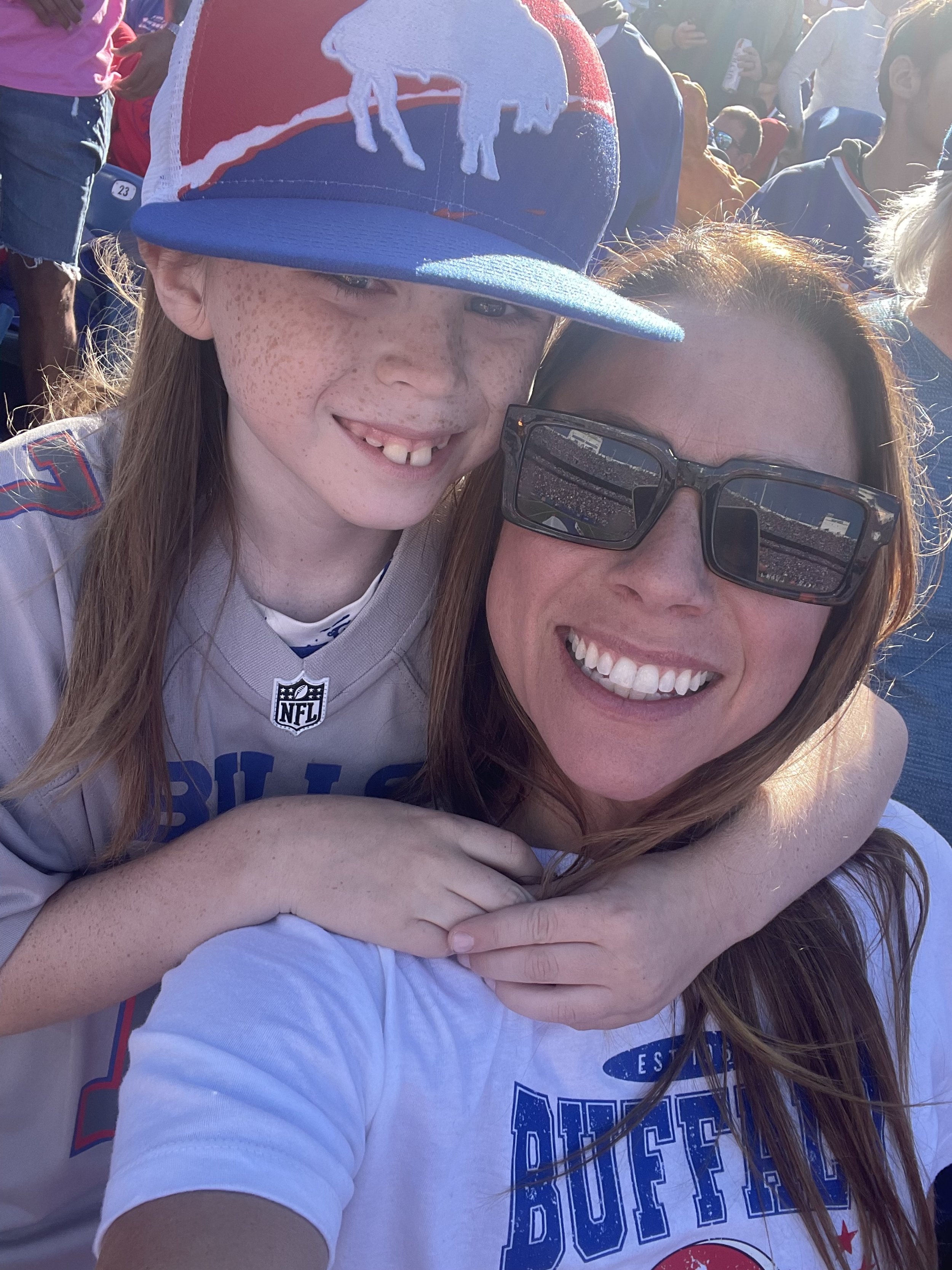 Two people smiling at a Buffalo Bills game, one wearing a jersey and a hat with Bills logo, and the other in a Bills t-shirt.