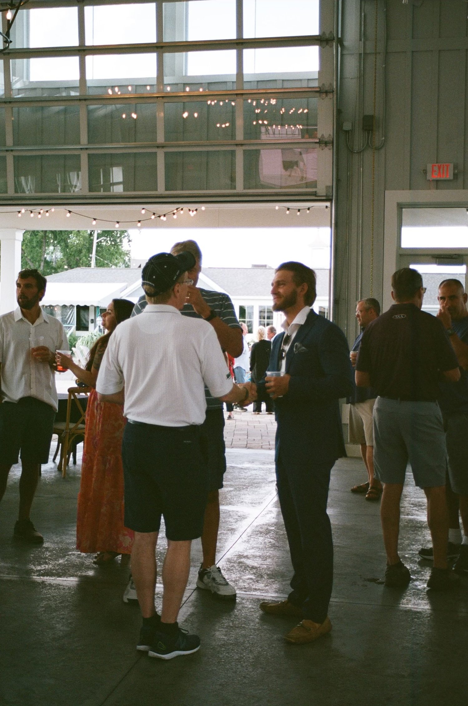 People socializing at an indoor event with string lights overhead.