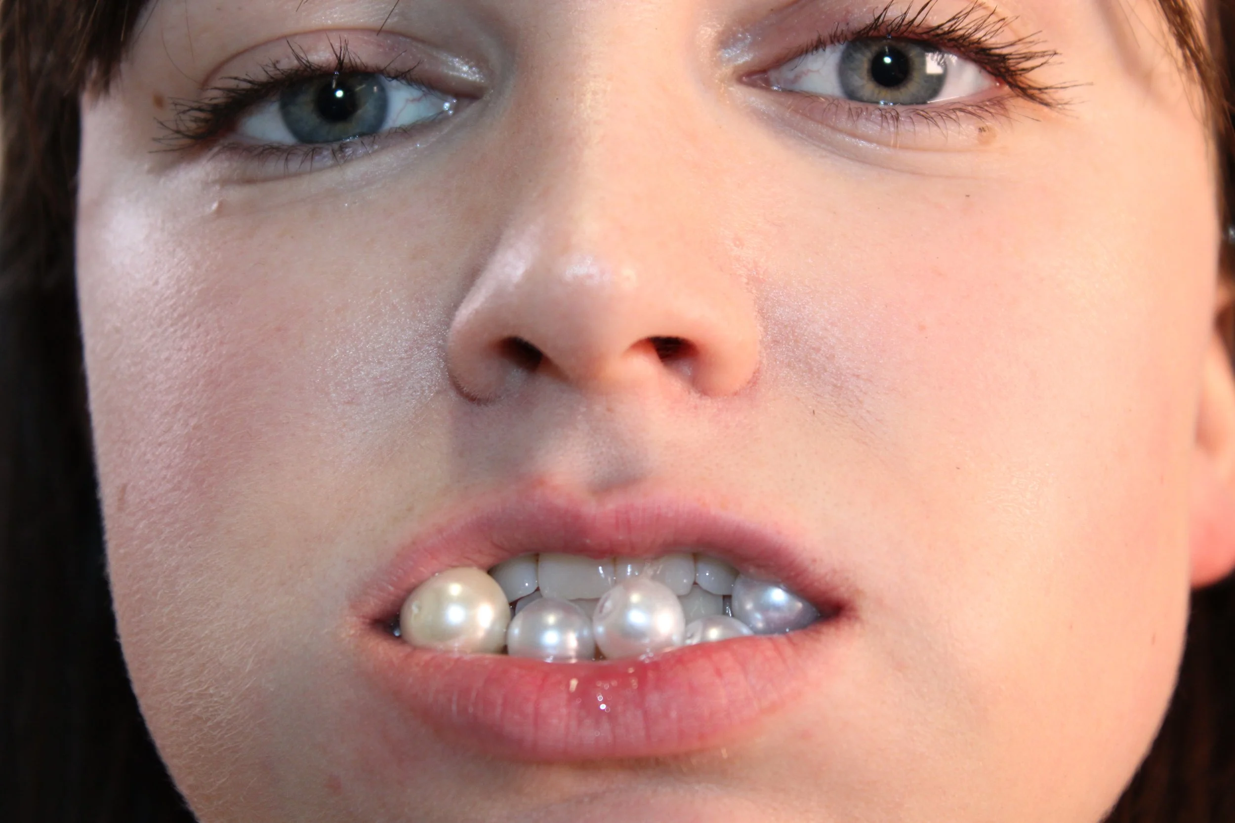 close up of a female face, grey eyes and a mouthful of pearls