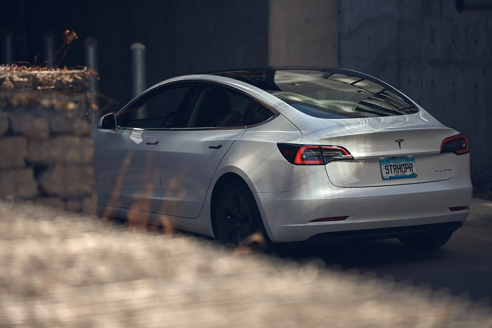 A silver Tesla Model 3 parked in an indoor area with concrete walls, with focus on the rear and side of the vehicle.