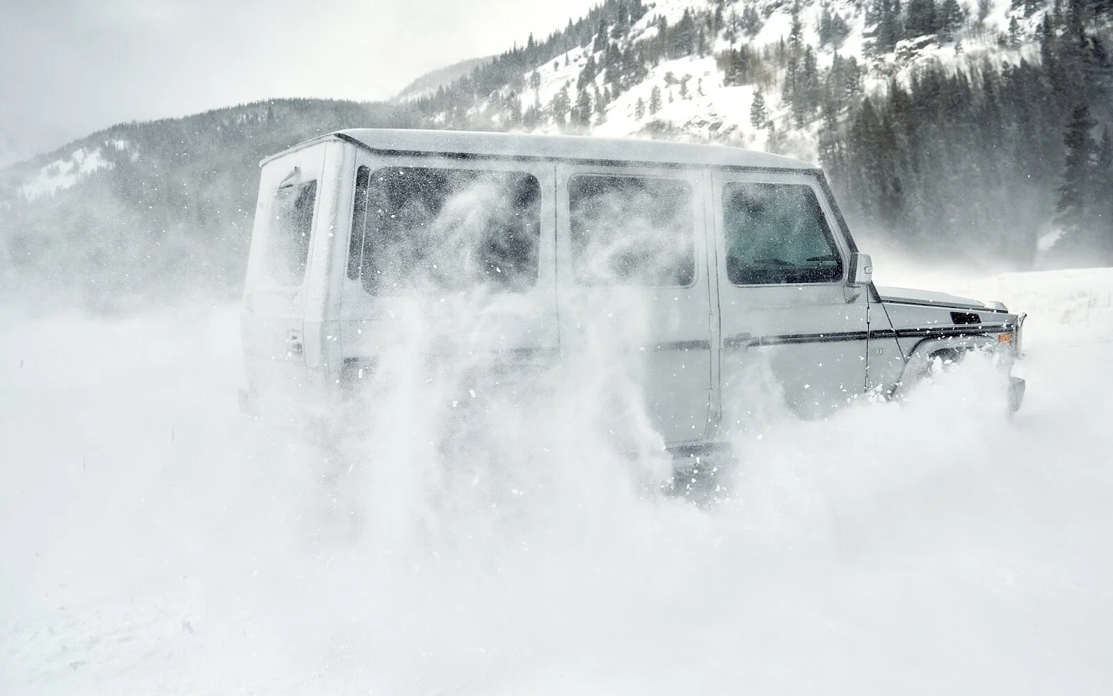 A silver SUV driving through deep snow in a mountainous winter landscape