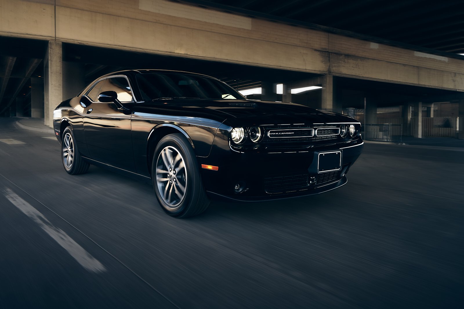 Black Dodge Challenger sports car driving through an urban underpass.