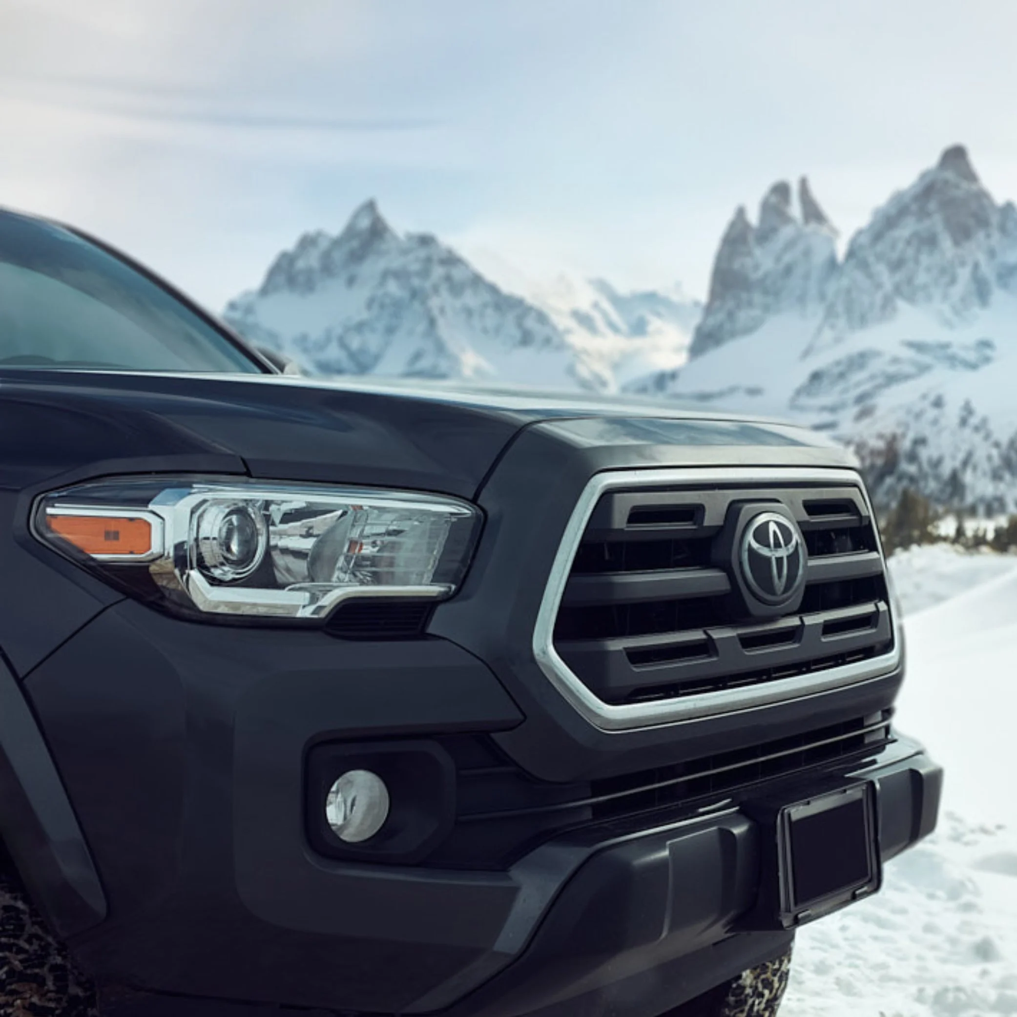 Black Toyota truck with snow-covered mountains in the background.