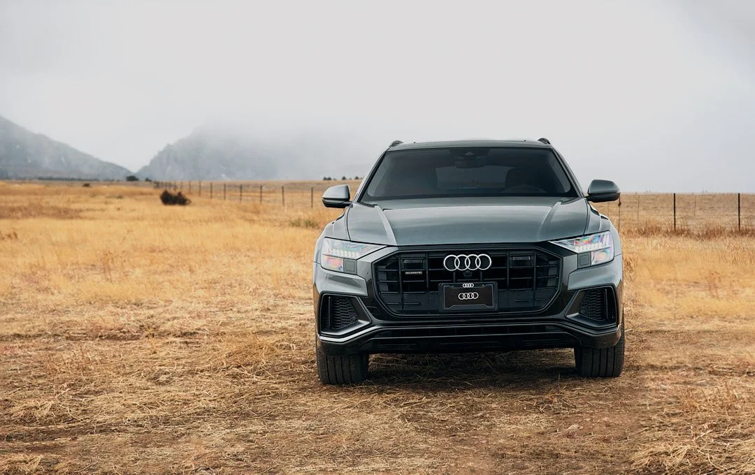 Front view of a black Audi SUV parked in a dry, open field with mountains in the background.