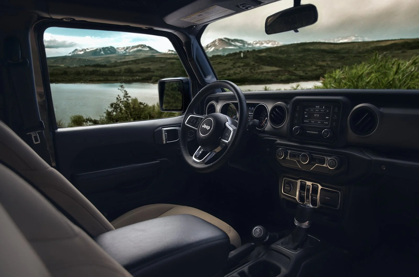 Interior of a Jeep vehicle with a view of a lake, mountains, and greenery through the windshield.
