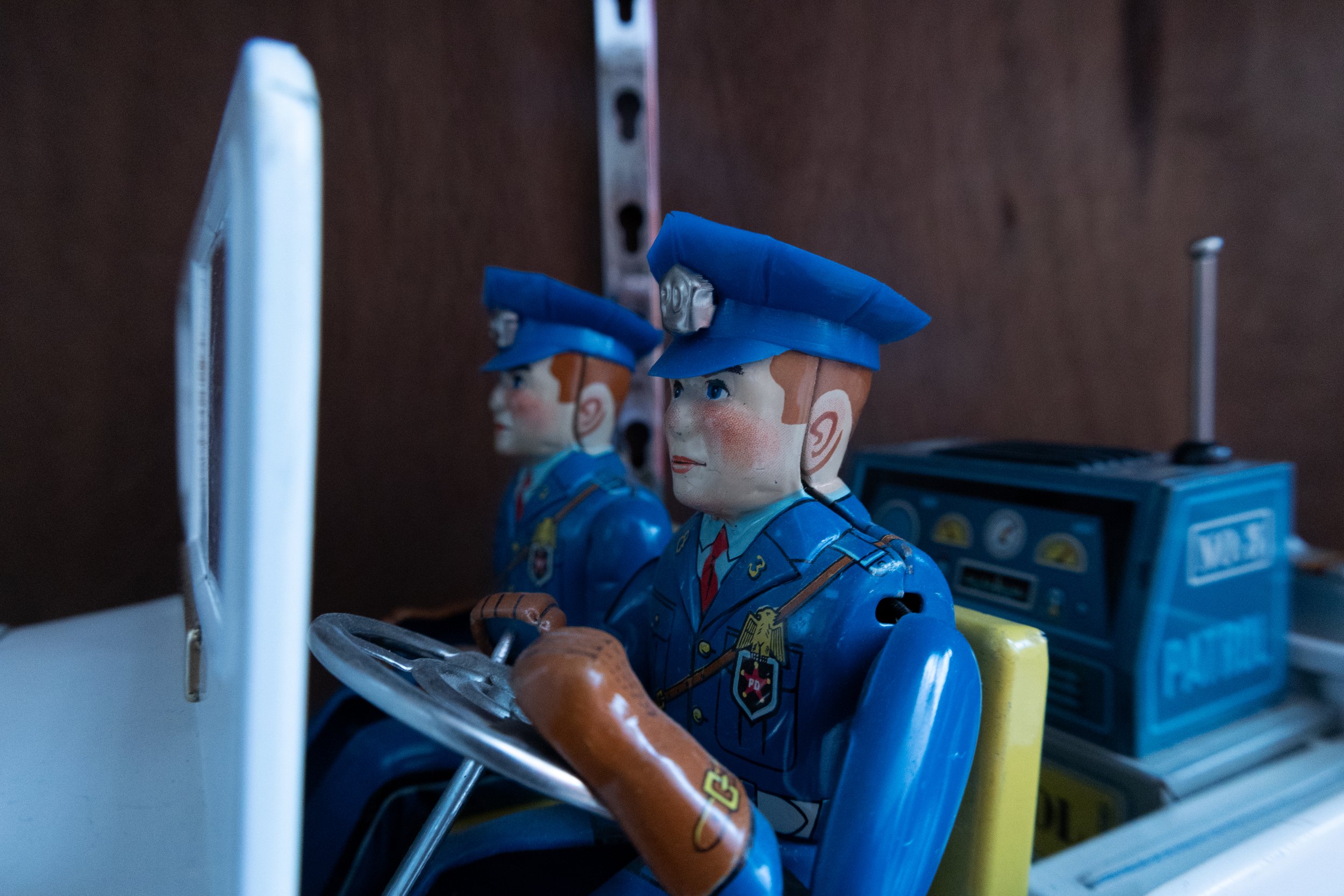 Twee vintage speelgoedpolitieagenten figurines van hout, gekleed in blauwe uniformen en hoofddeksels, naast een speelgoedradio en andere speelgoed items.