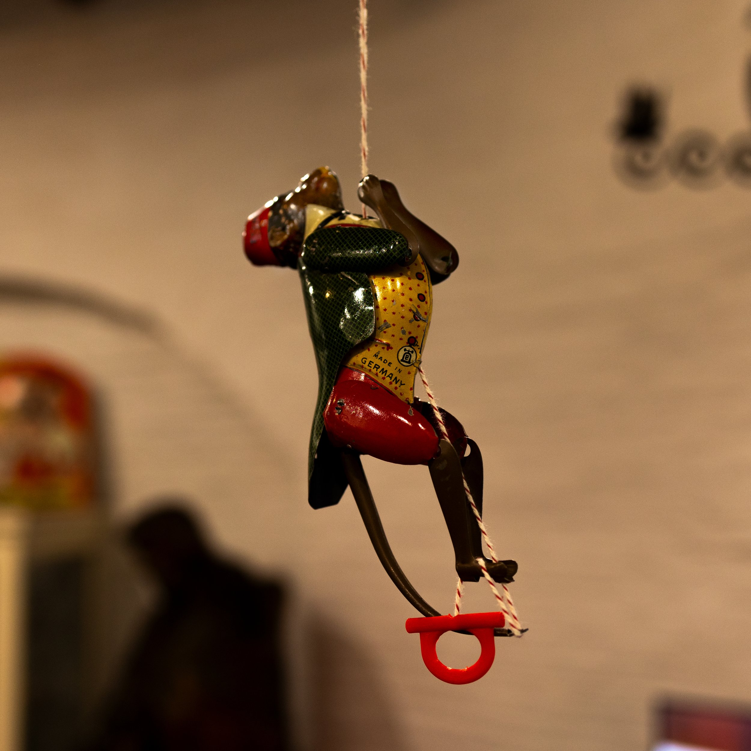 Een hangende speelgoedfigurine die een danseres voorstelt, gemaakt van metalen onderdelen en gekleurd met verf, met een rode schommel onder haar voeten.
