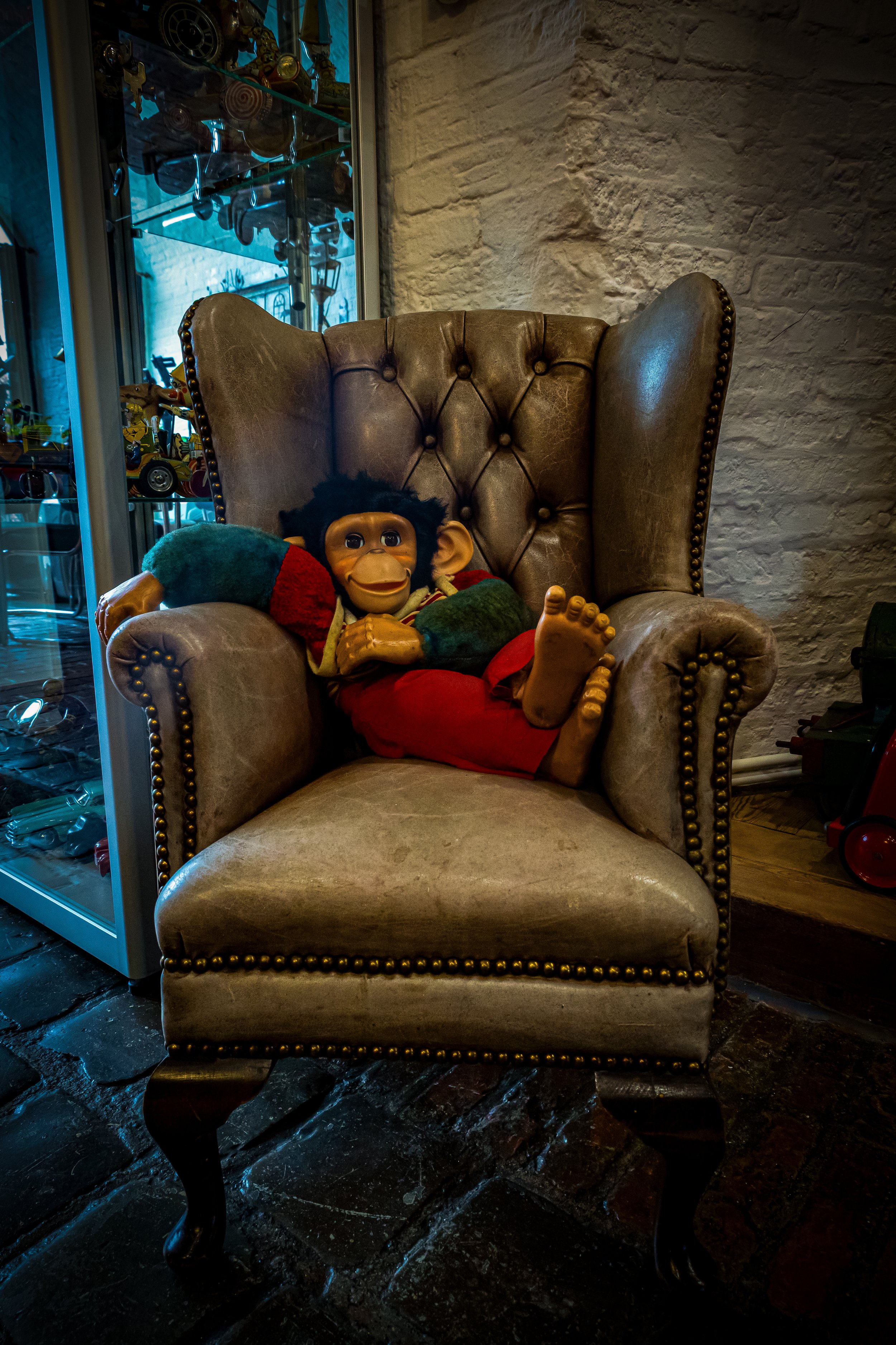 Een knuffelpop van een aapje liggend op een grote, landelijke fauteuil met leren bekleding, in een vintage interieur.