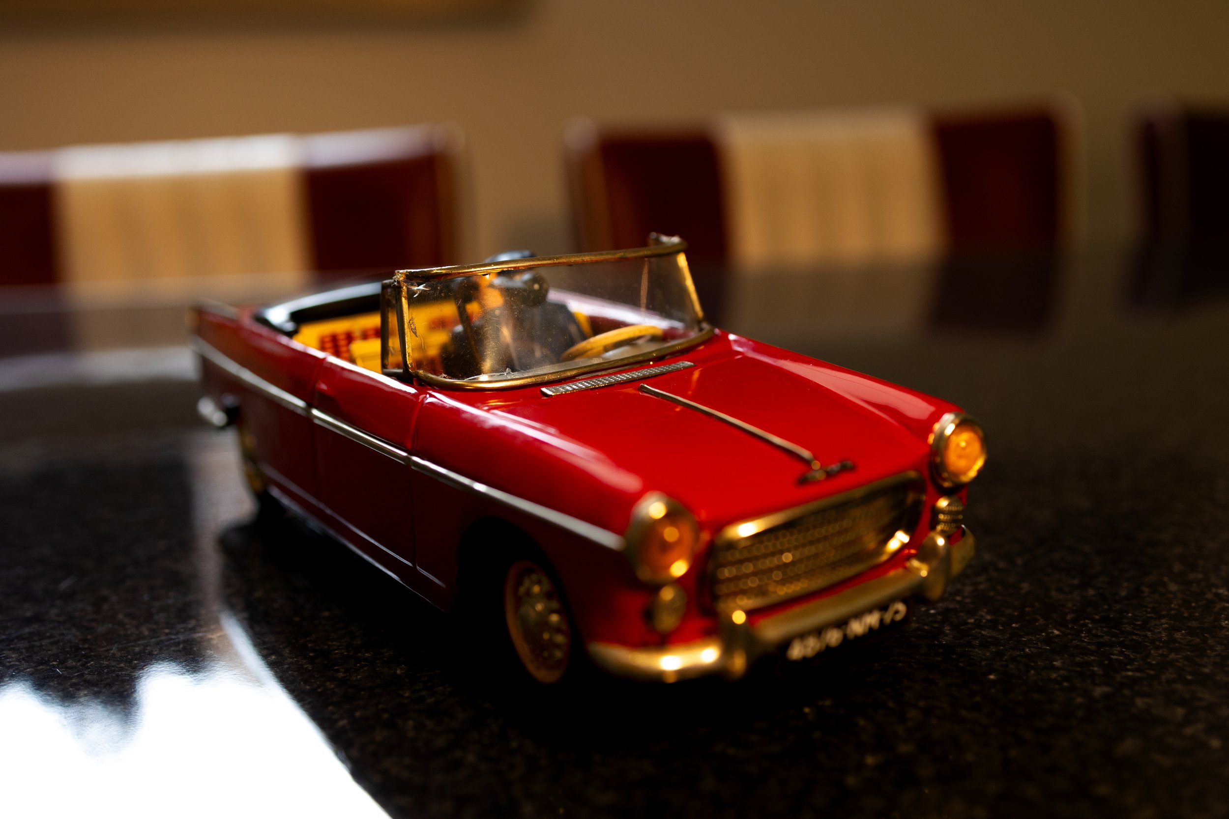 Een klein rood model van een klassieke cabrioletauto op een donkere tafel.