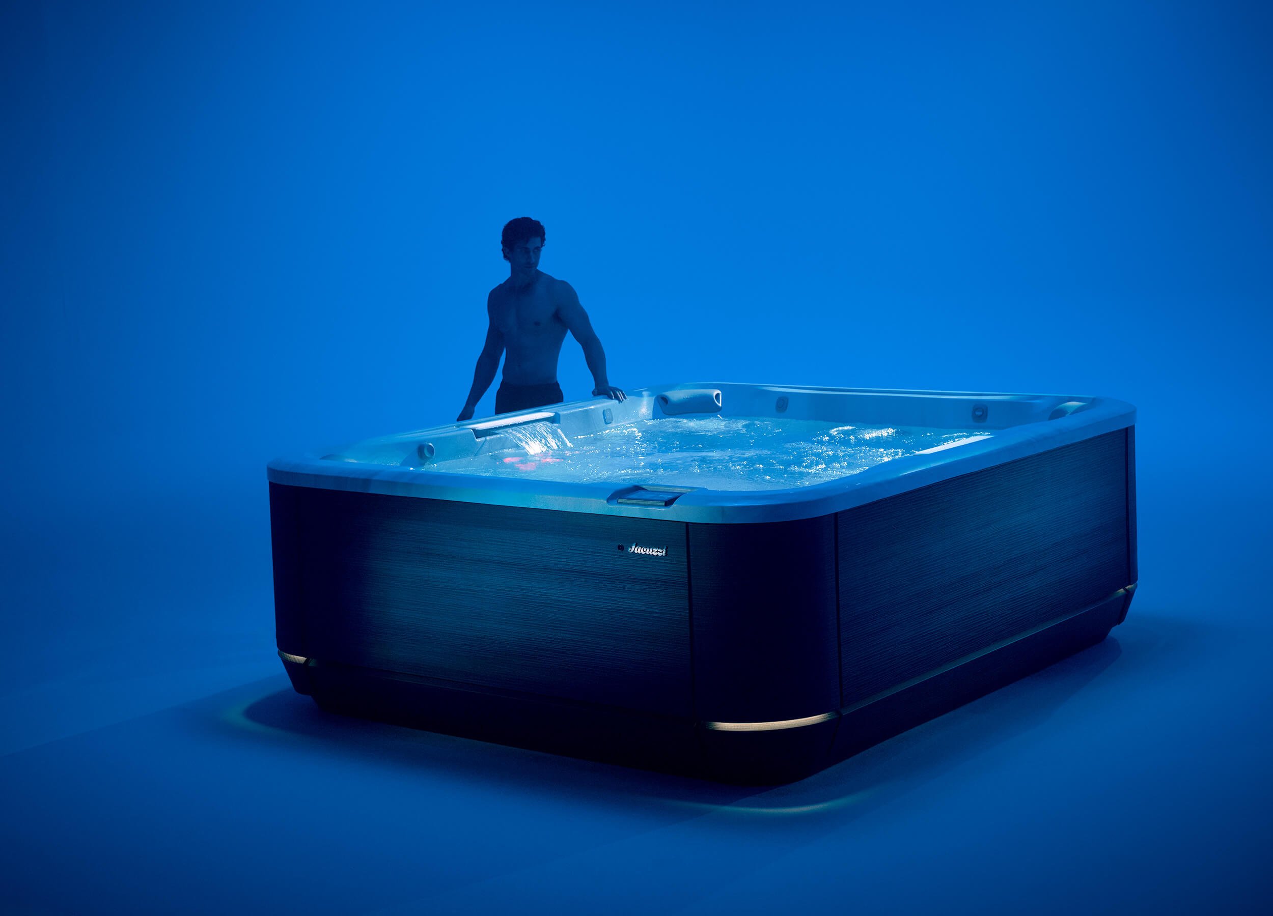 Moody blue-lit interior showroom with man standing next to Jacuzzi® J509™ Hot Tub.