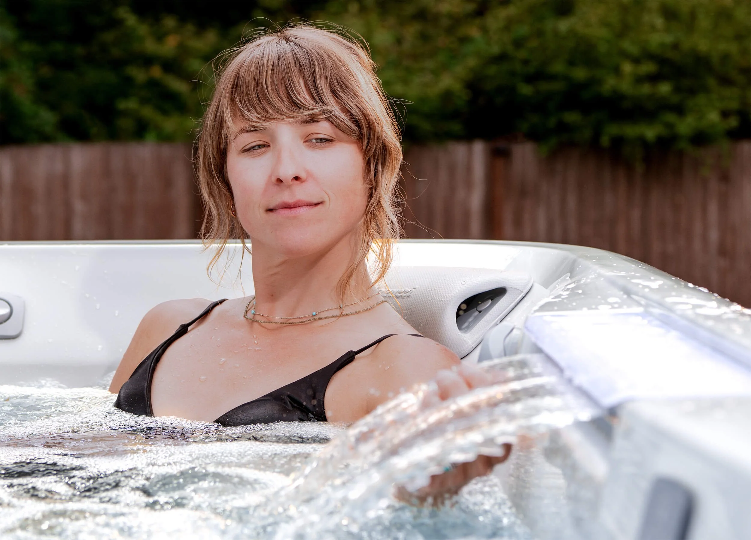 Woman relaxing in Jacuzzi® J508L Hot Tub in residential backyard setting with waterfall feature active in foreground.