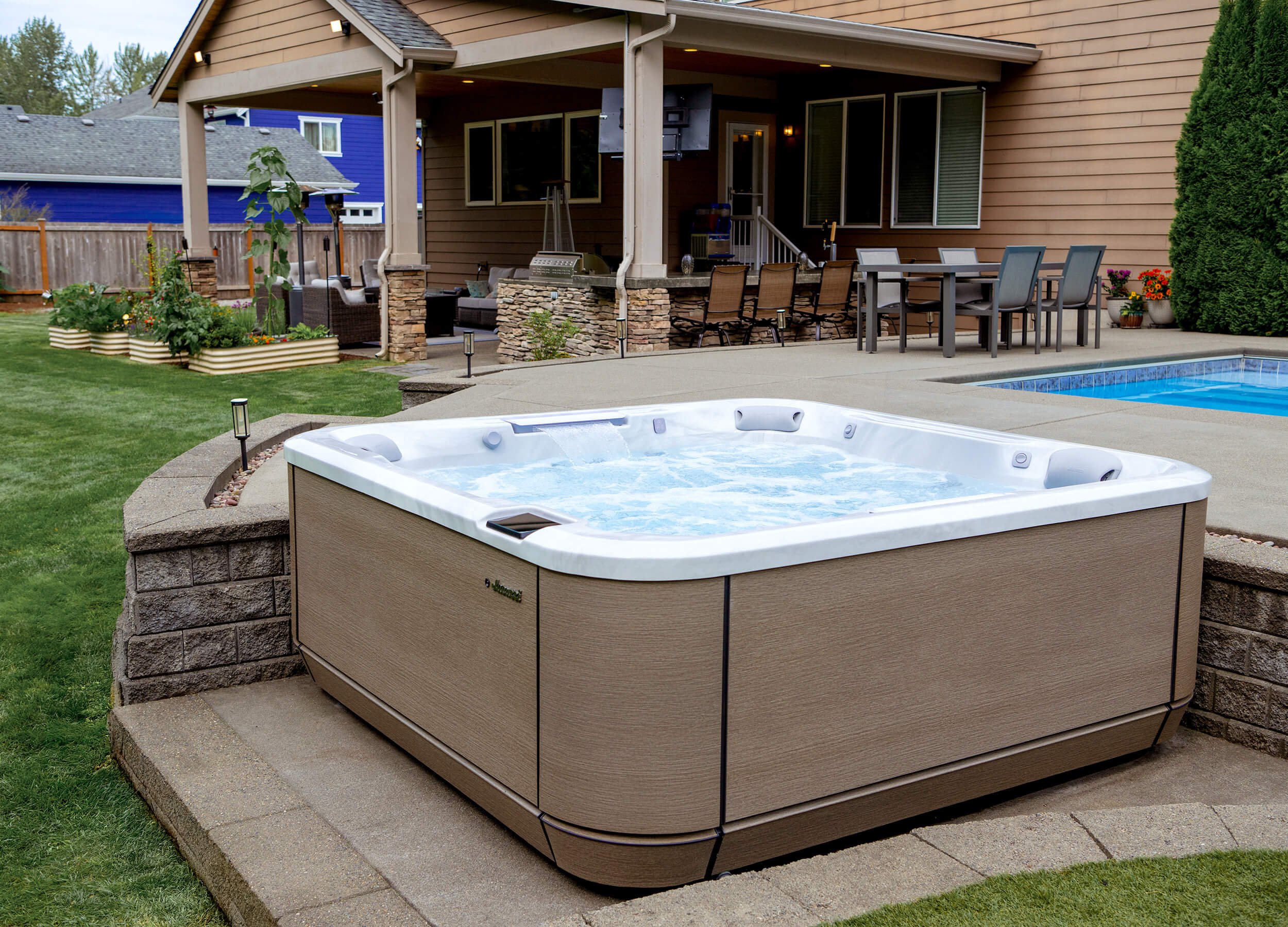 Product image- Jacuzzi® J-L508L hot tub on brick patio in residential backyard settring with grass and home in background.