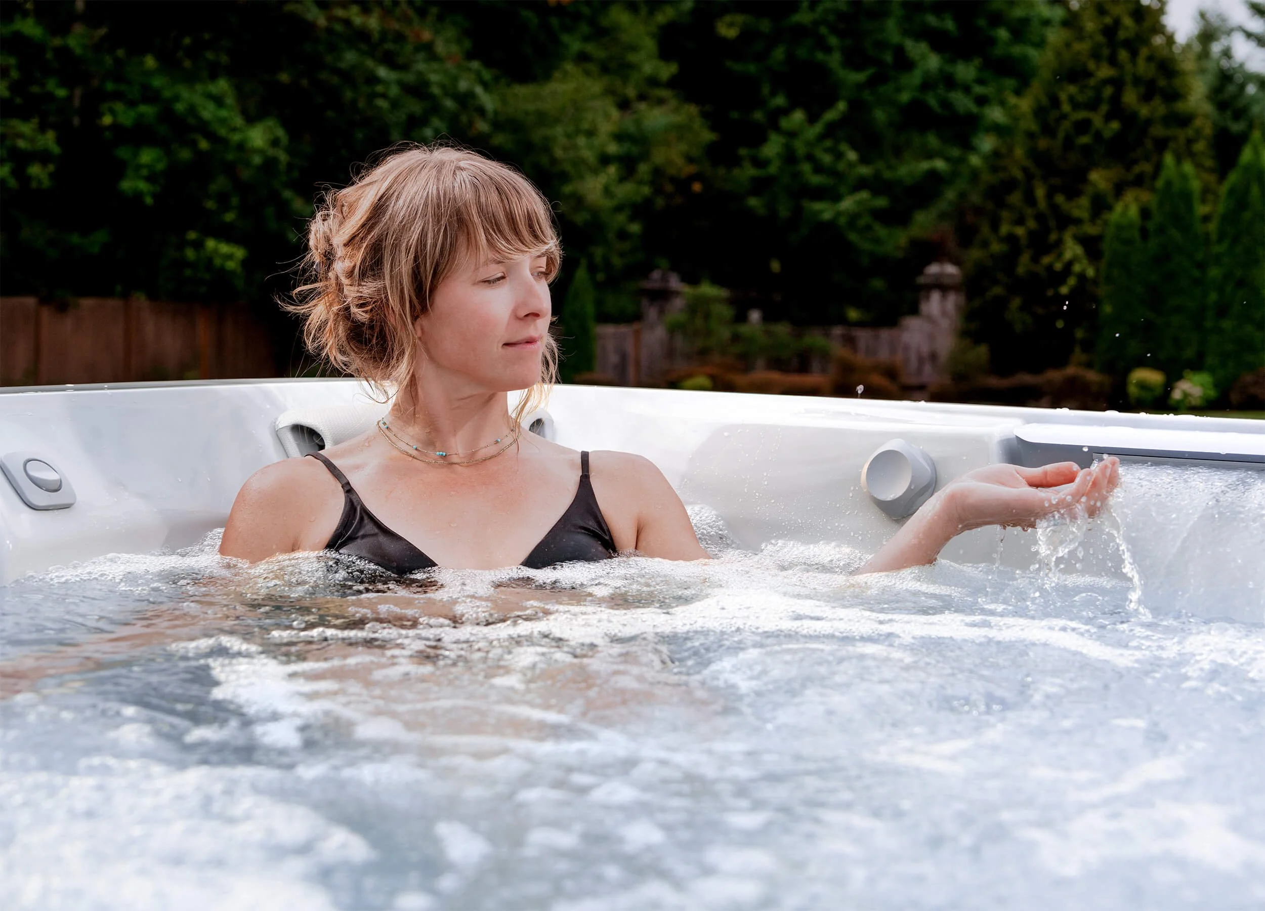 Woman in black bathing suit enjoying sitting in a Jacuzzi® J508L™ hot tub in a residential backyard setting.