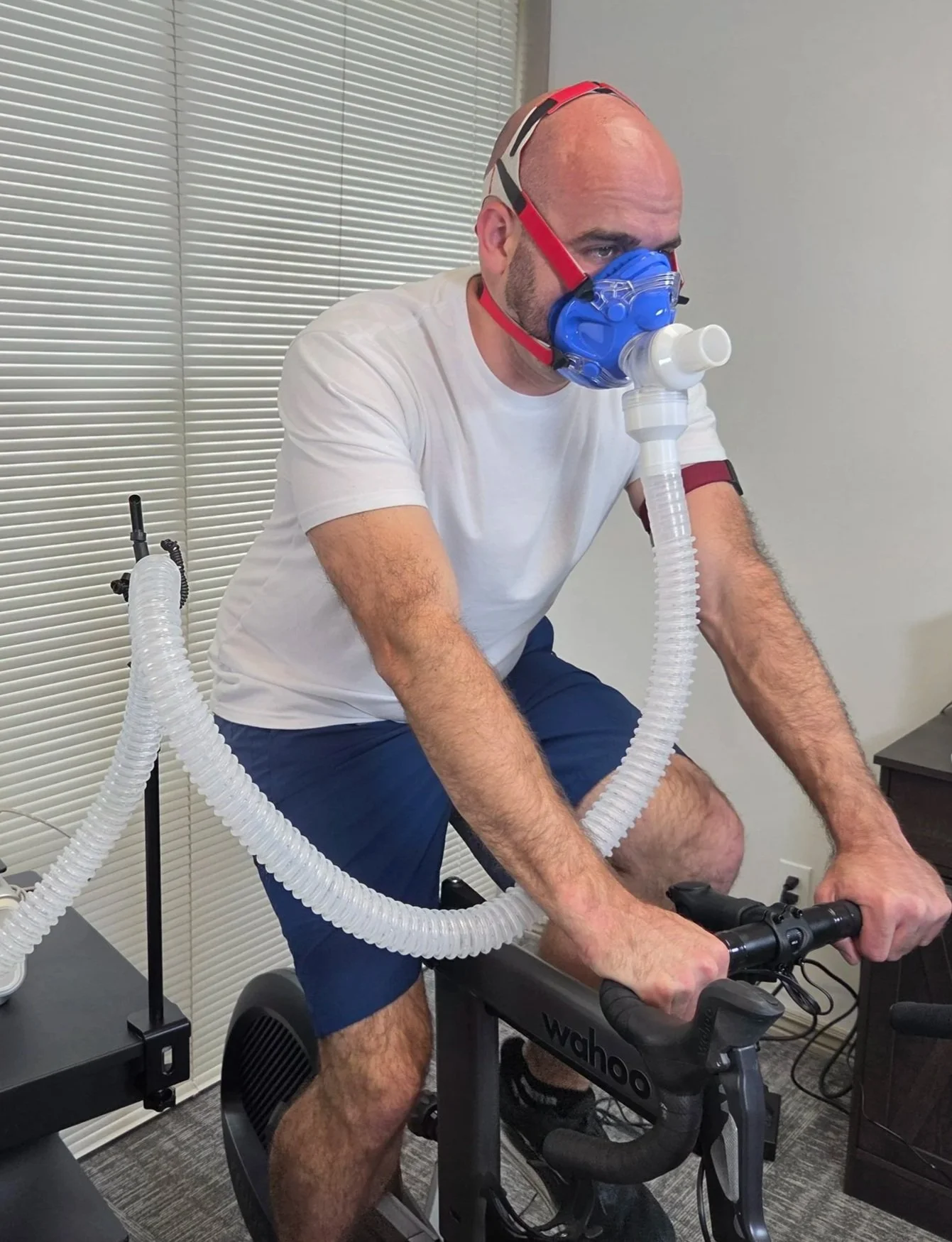 A cyclist wearing a metabolic analysis mask while performing a VO2 Max assessment on a stationary bike trainer to calculate power output and aerobic training zones