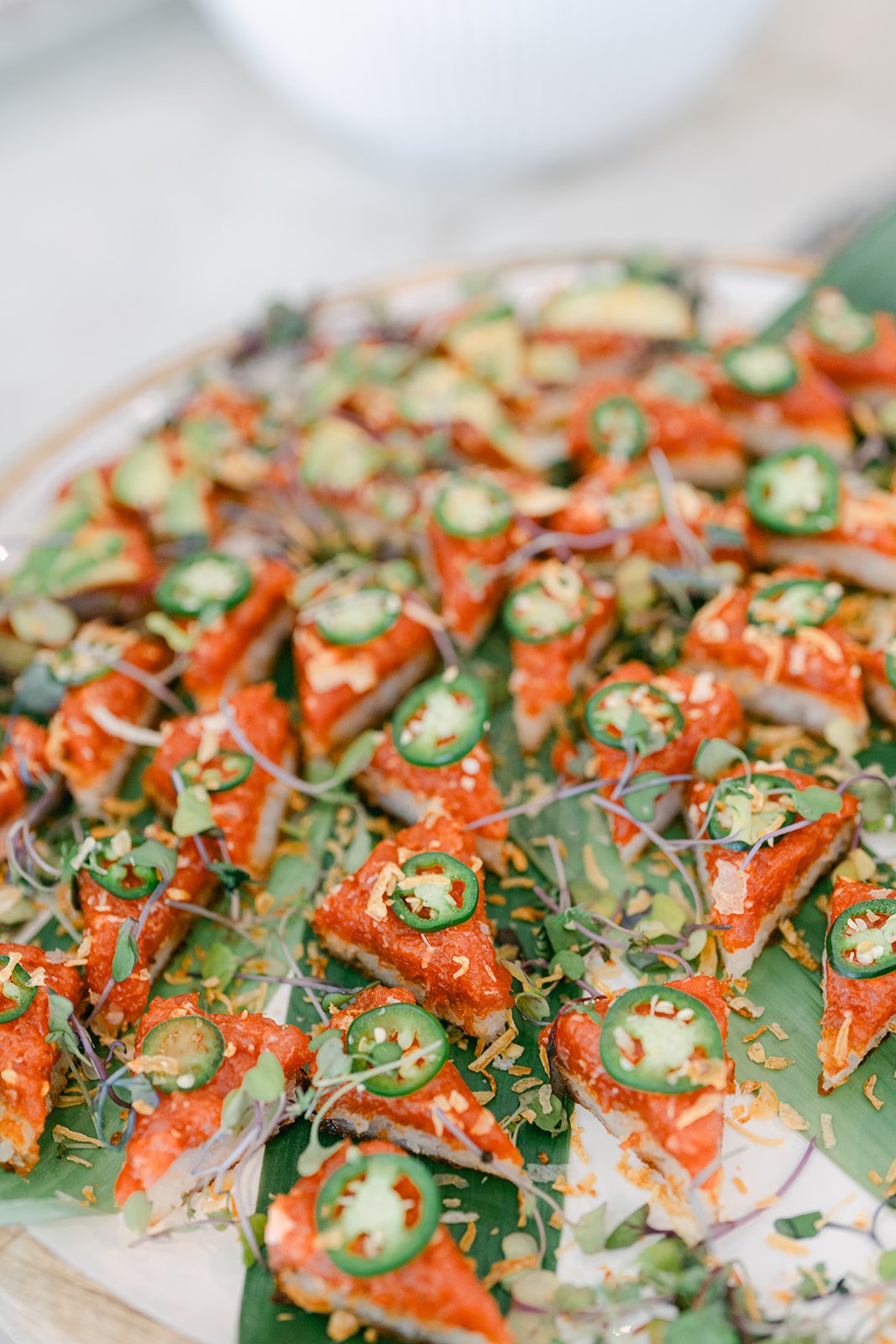 Sliced sushi rolls topped with sliced jalapenos, microgreens, and drizzled with sauces on a wooden platter.