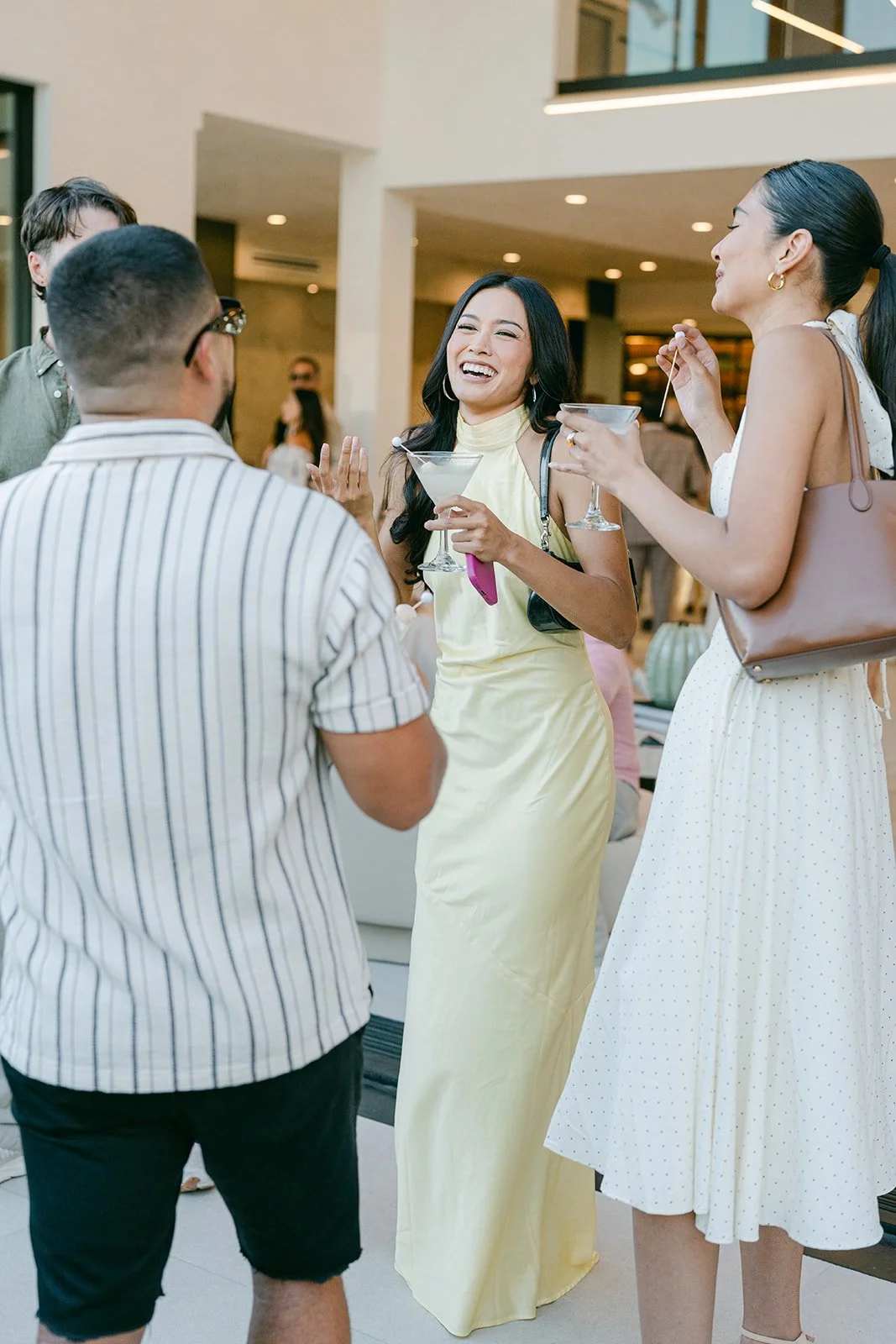 Group of four people talking and laughing at a social gathering indoors, holding cocktails.