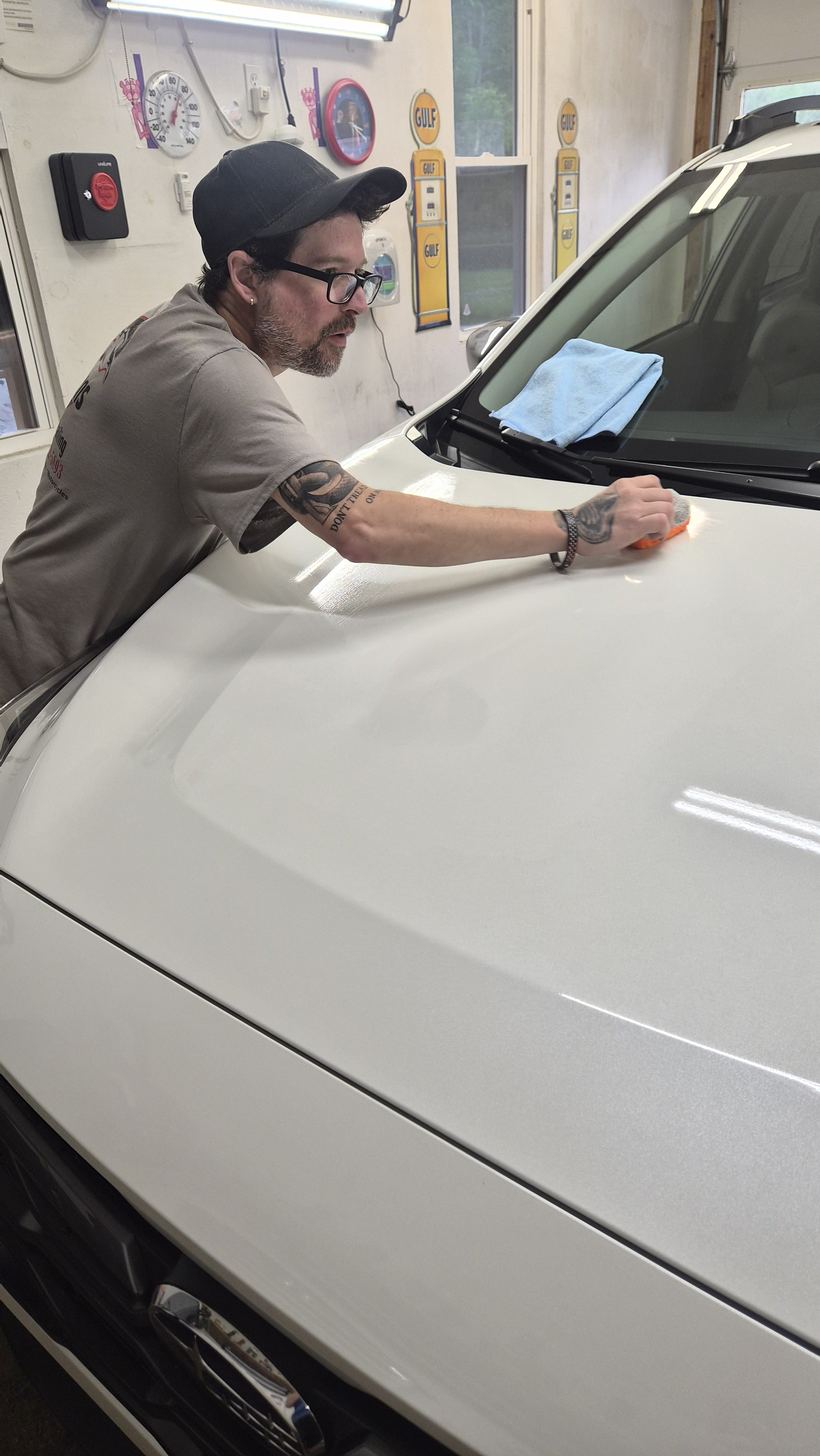 Man applying Ceramic Coating to the hood of a white car inside a garage.