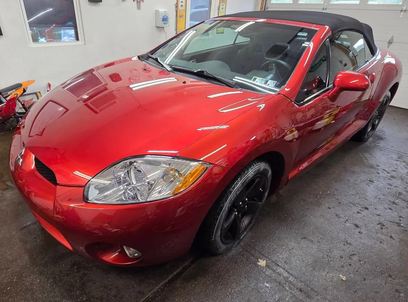 Red convertible car with black wheels parked inside a garage.