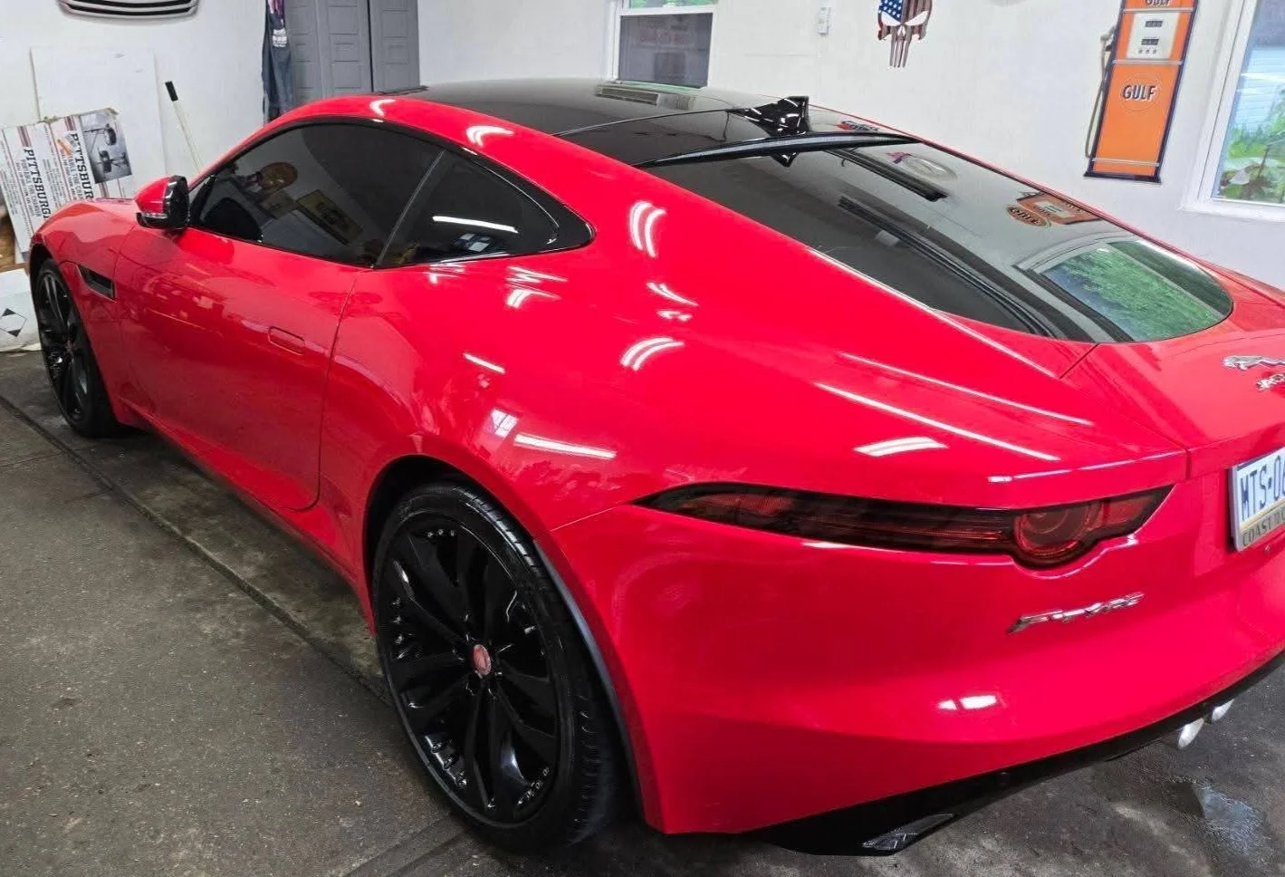 Red sports car with black racing stripes, parked indoors with reflections of the garage lights on its shiny surface.