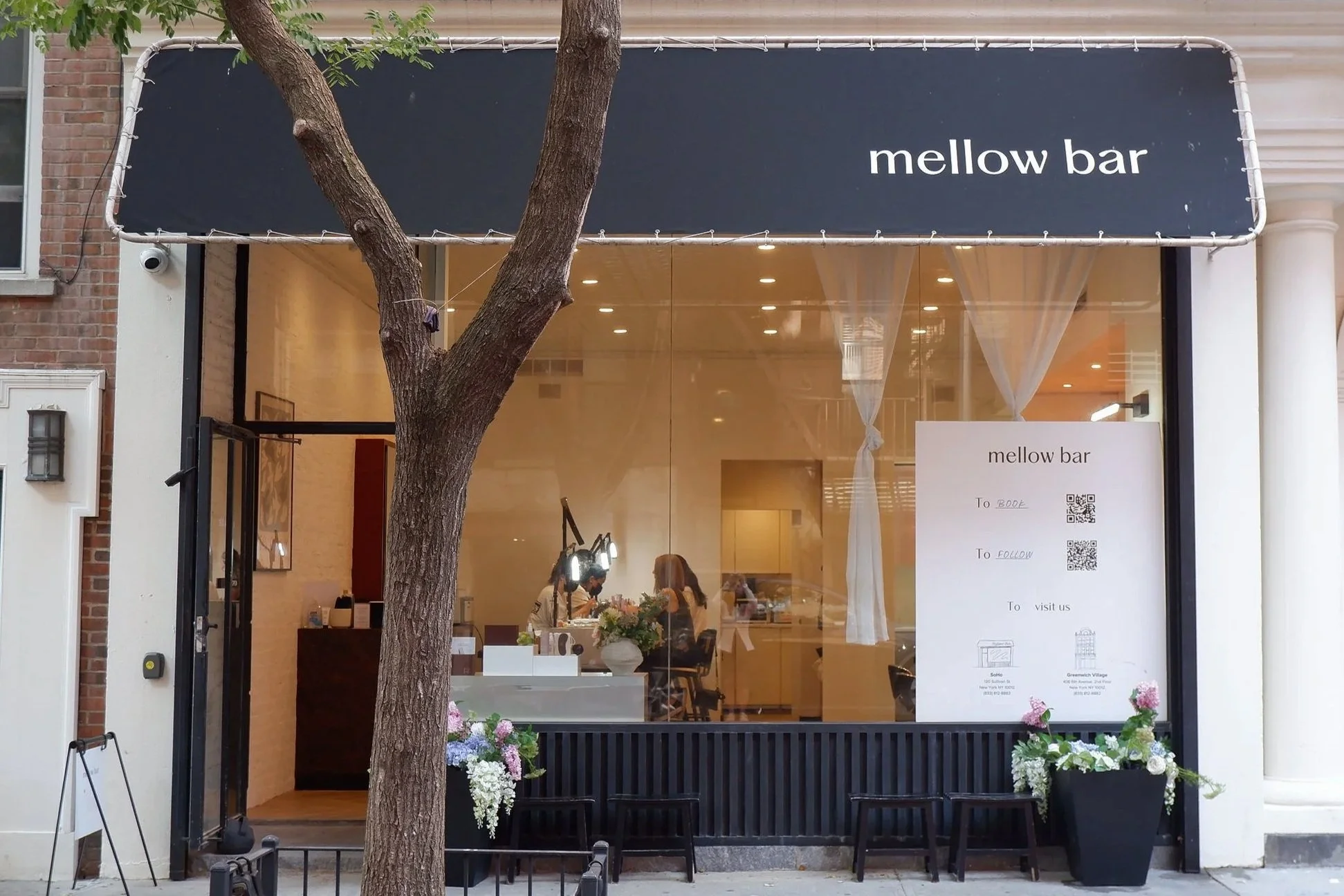 Exterior view of Mellow Bar's location in SoHo, New York, featuring a black awning, large glass windows, and the nail salon's modern minimalist interior visible from the street.