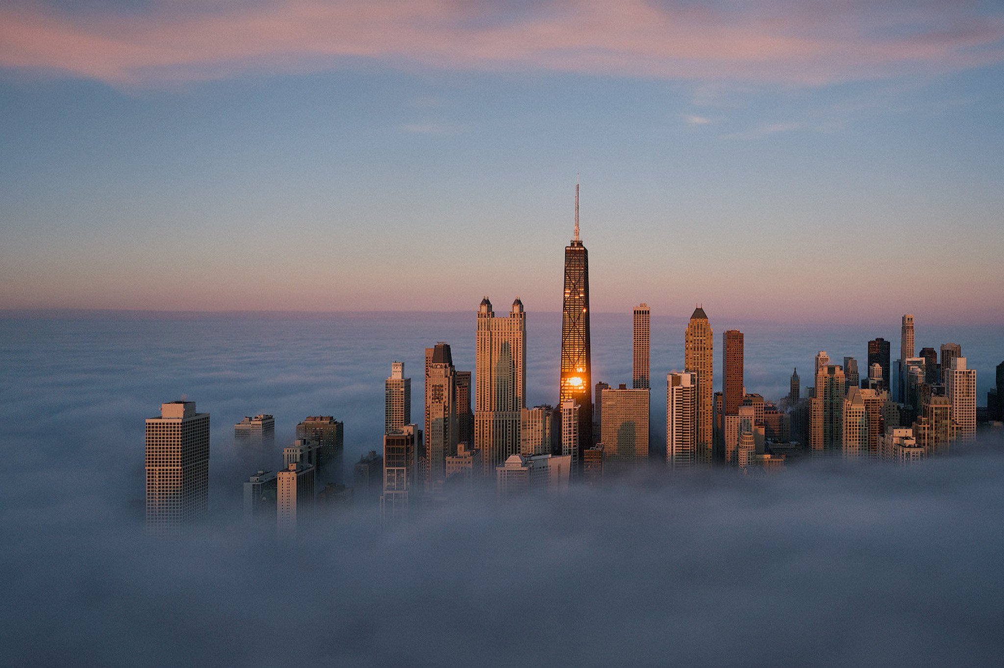 Chicago's John Hancock Tower emerges above a blanket of clouds at dusk, a symbol of the city's towering ambition and serene beauty.