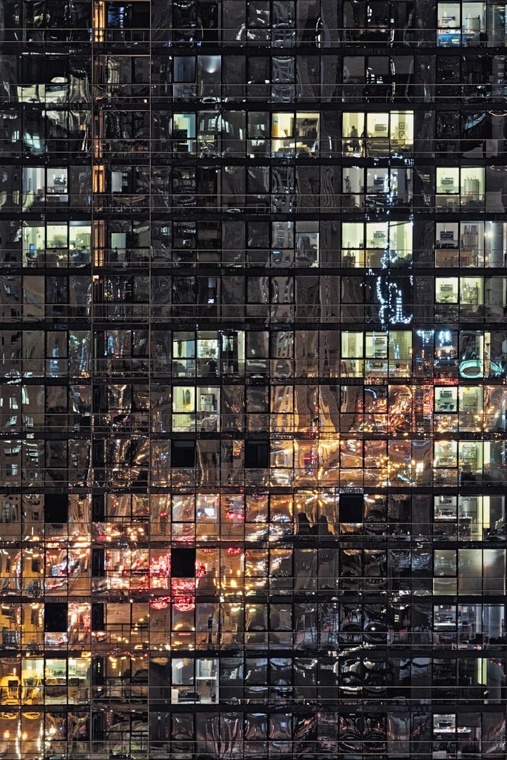 Close-up night view of a skyscraper's facade showcasing illuminated office windows and reflections of city lights.