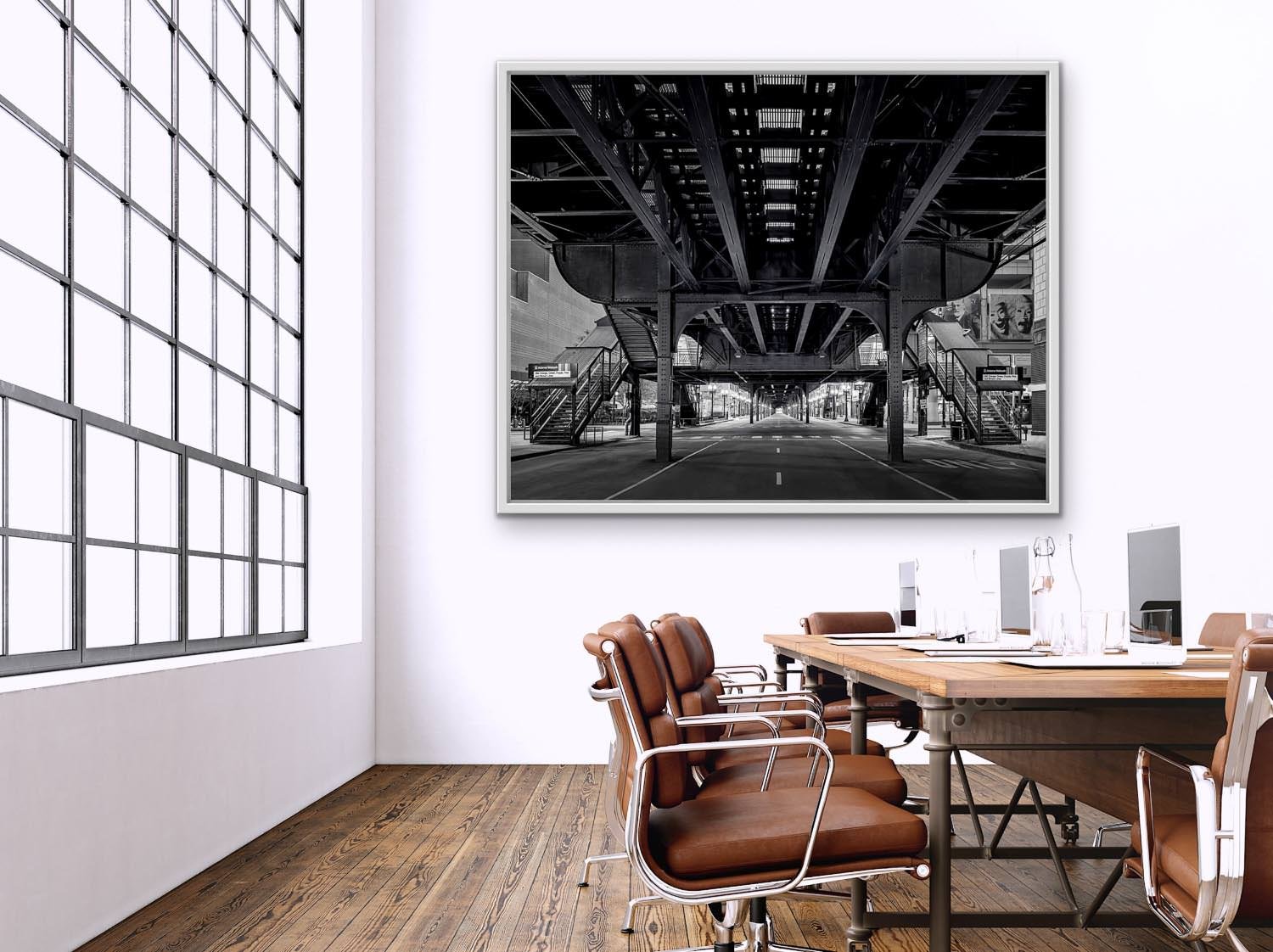 Elevated train tracks in grayscale over an empty Chicago street with staircases on either side and city lights casting shadows.
