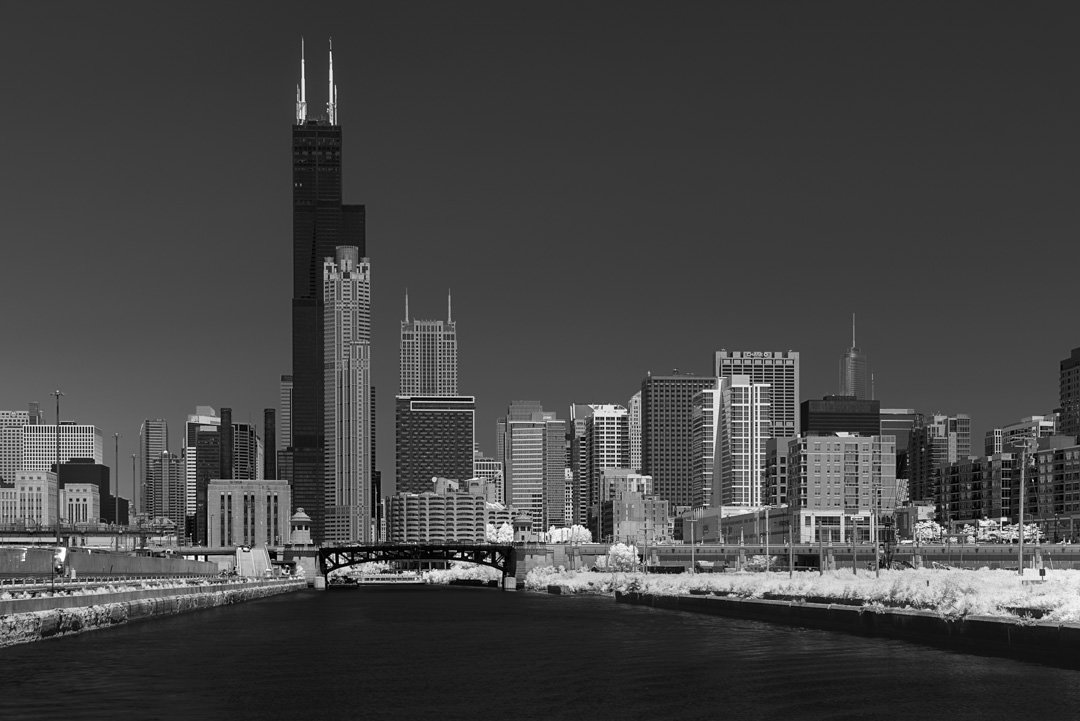 Monochrome view of Chicago's skyline with Willis Tower prominent, a bridge over the river in the foreground.