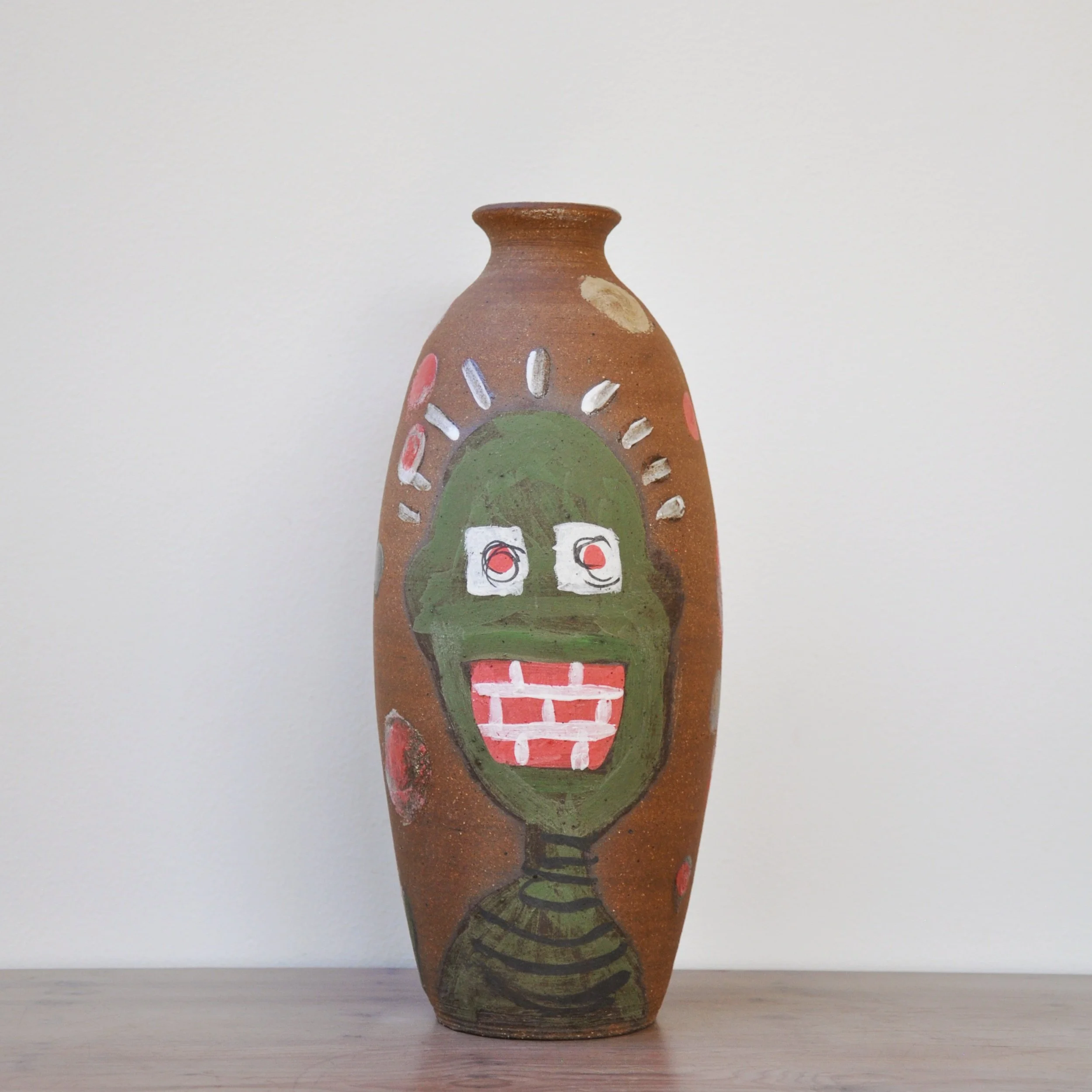 Tall brown ceramic vase with abstract face painting in green, white, and red colors.