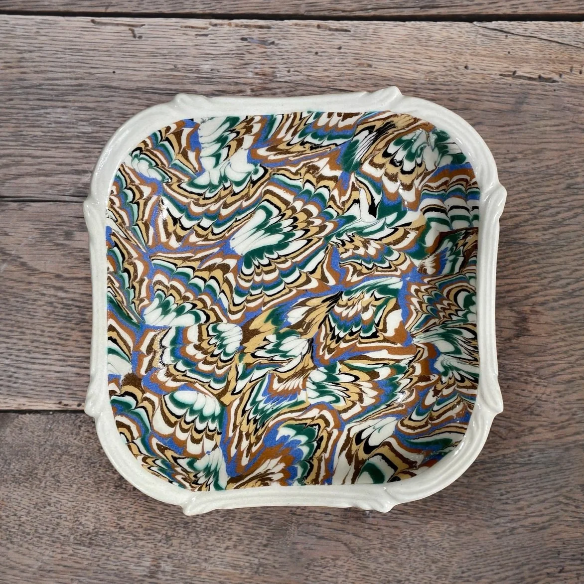 Colorful marbled rectangular ceramic dish with abstract pattern, placed on wooden surface.