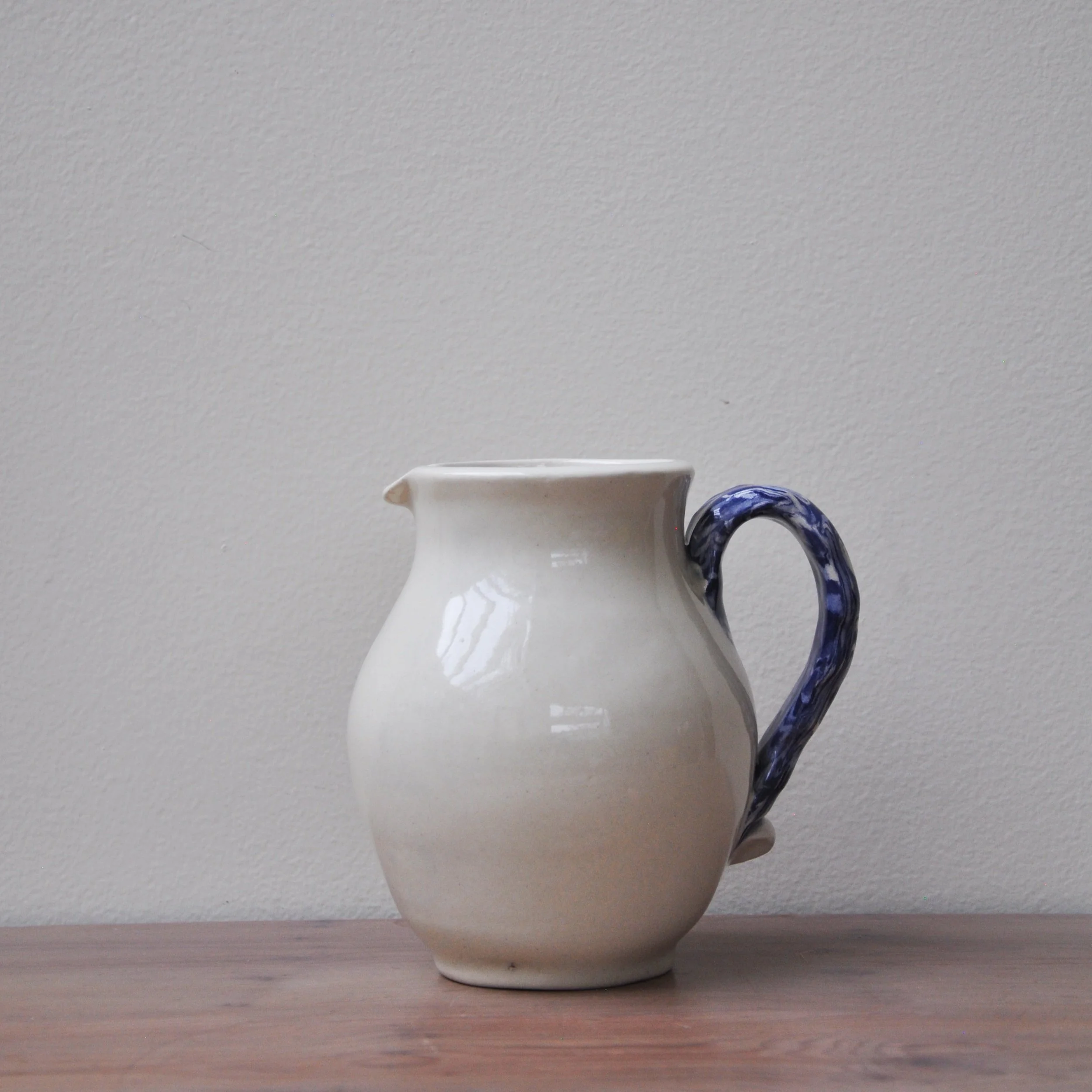 White ceramic pitcher with blue handle on a wooden surface