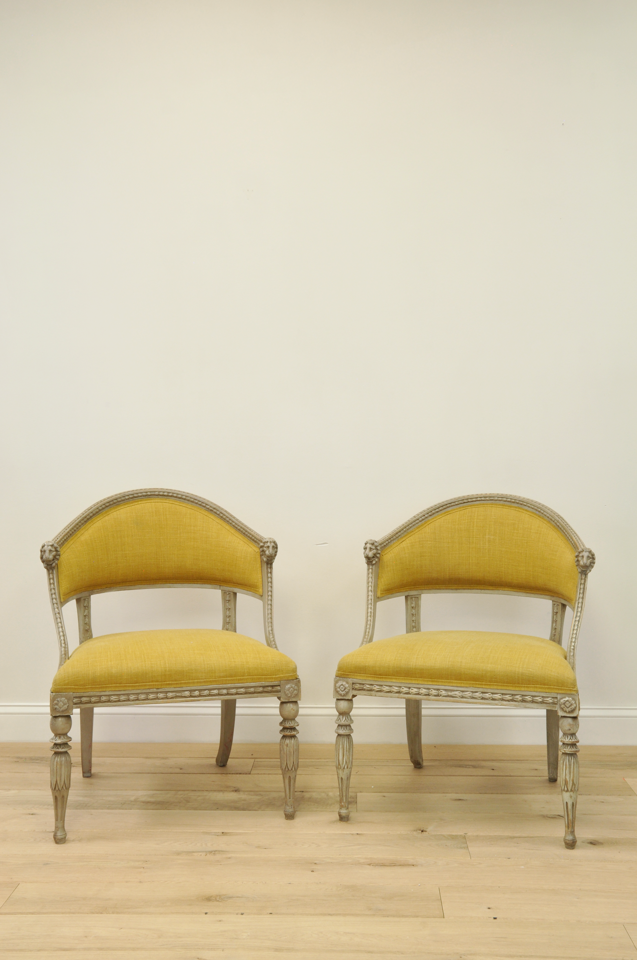 Two vintage yellow upholstered chairs with ornate wooden frames, set against a plain white wall on a light wooden floor.
