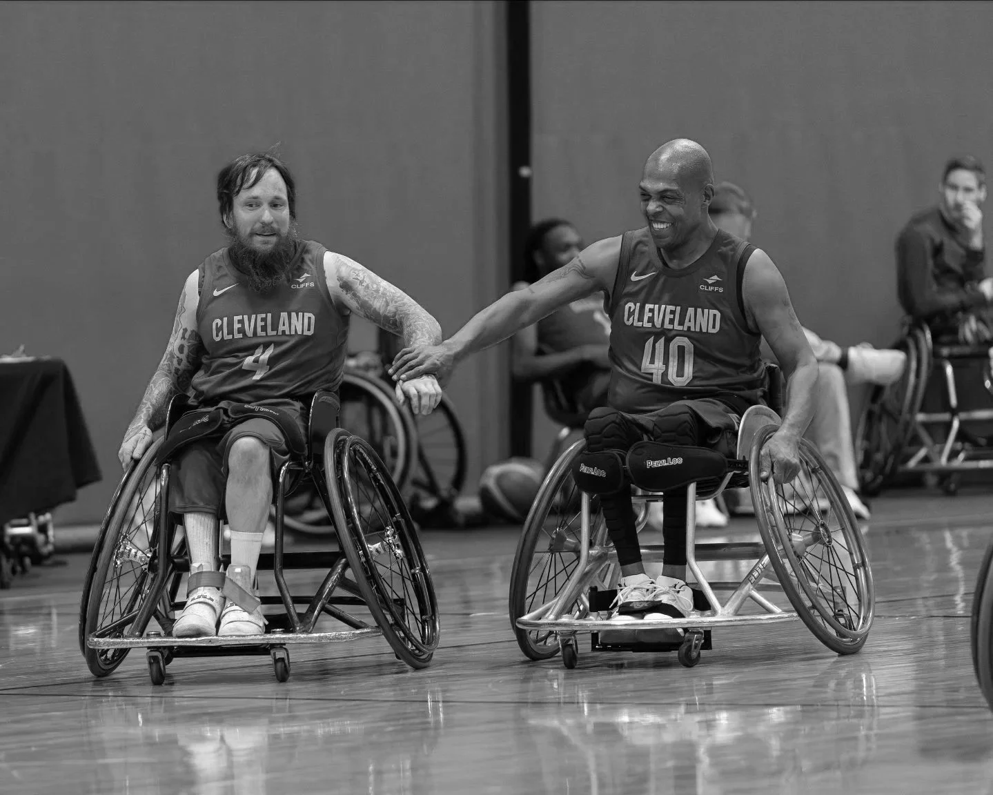 Two male wheelchair basketball athletes giving each other a high five while smiling.