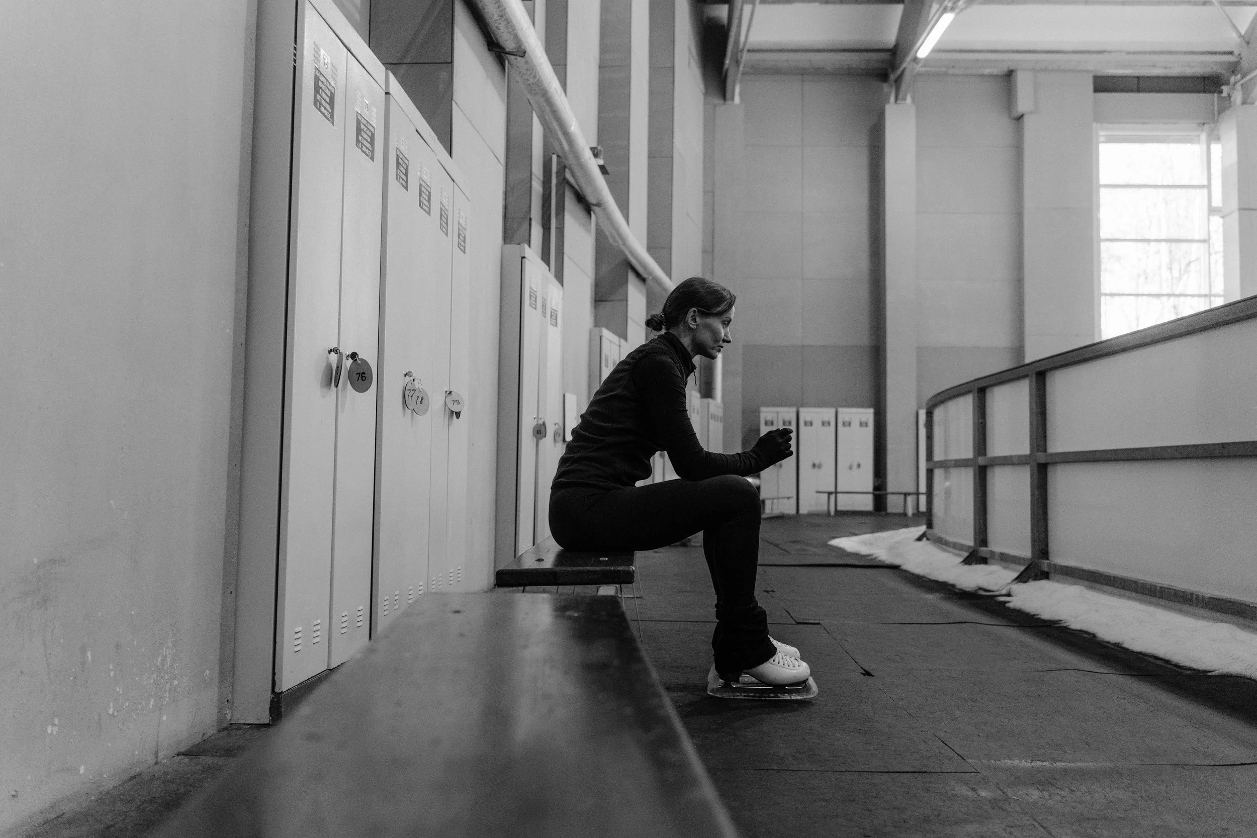 Female ice skater sitting on a bench in front of her locker.