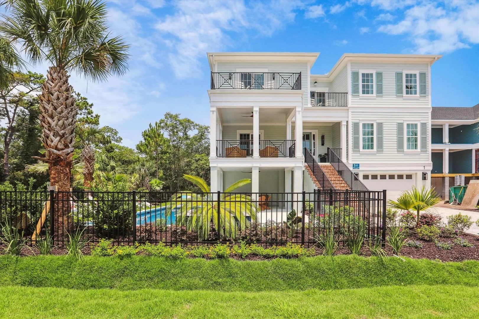 green three story beach house with stairs leading up to it, a pool, and landscaping out front.