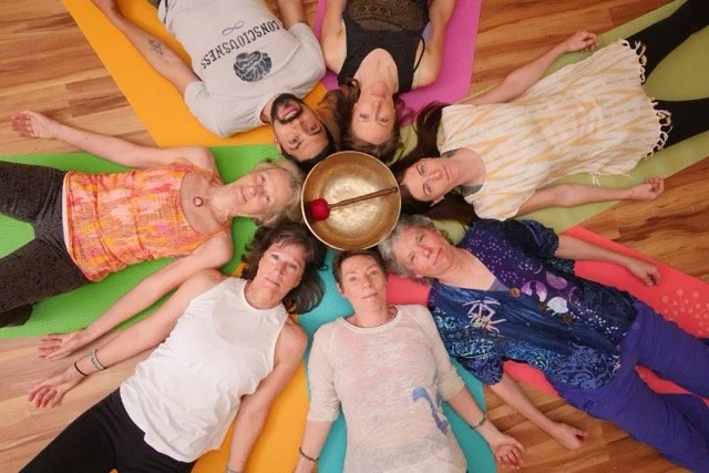 A group of yoga teachers laying down around a singing bowl, colorful and happy mood