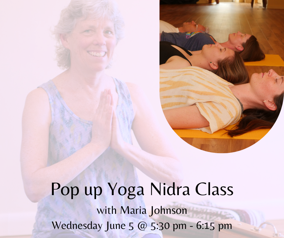 A smiling woman practicing yoga in a class, with three people lying on yoga mats on the floor behind her, during a yoga session.