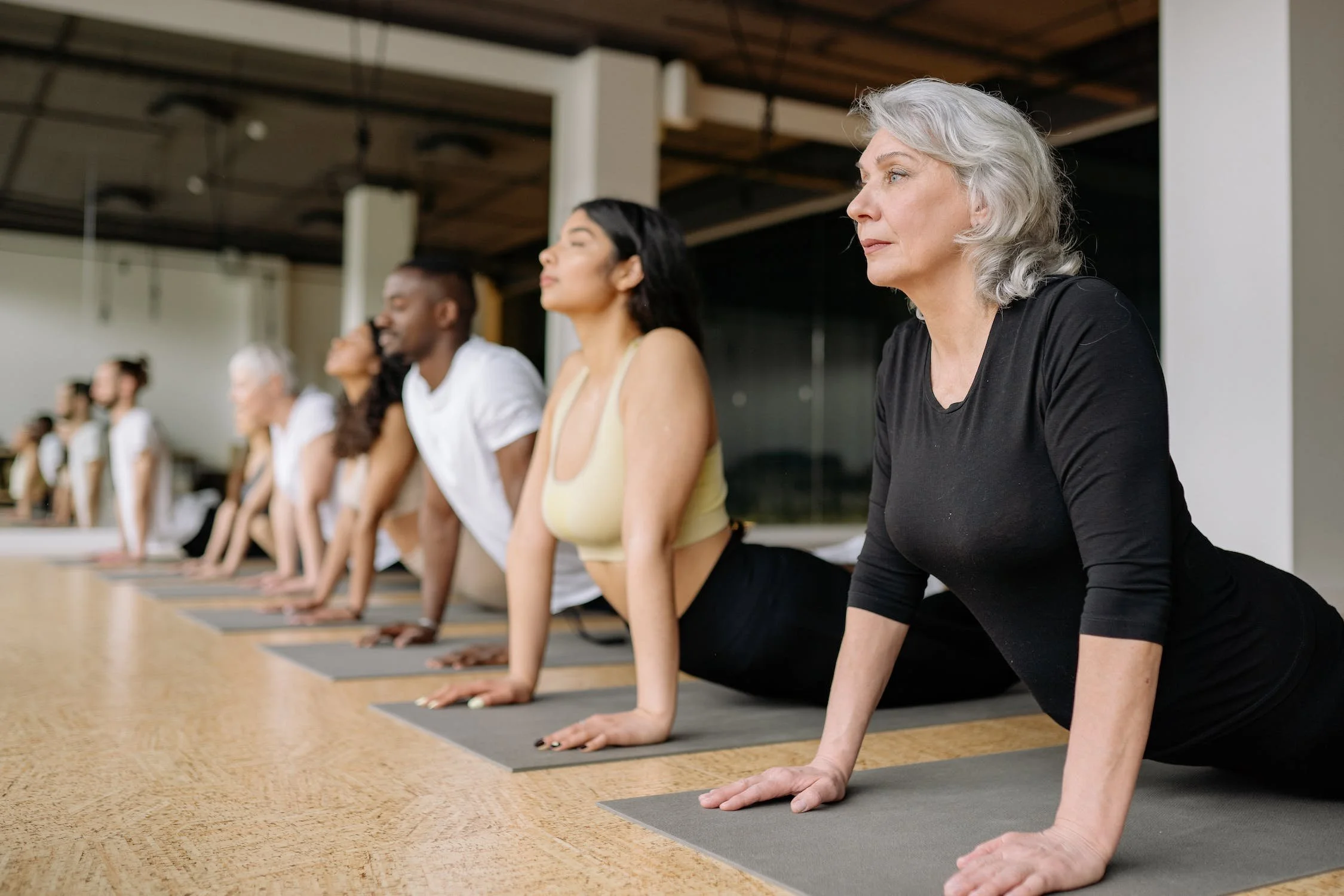 A diverse group of people doing yoga in a studio, in a cobra pose, focusing forward with eyes closed or looking ahead.